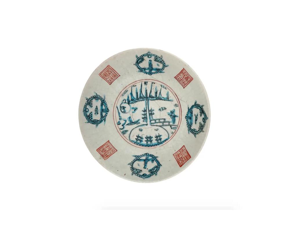 Ancienne assiette ou chargeur en porcelaine bleue et blanche peinte à la main à l'époque Meiji. Circa : fin du 19e siècle au début du 20e siècle. Le chargeur est orné d'une image peinte à la main d'un paysage marin rural entouré de médaillons bleus