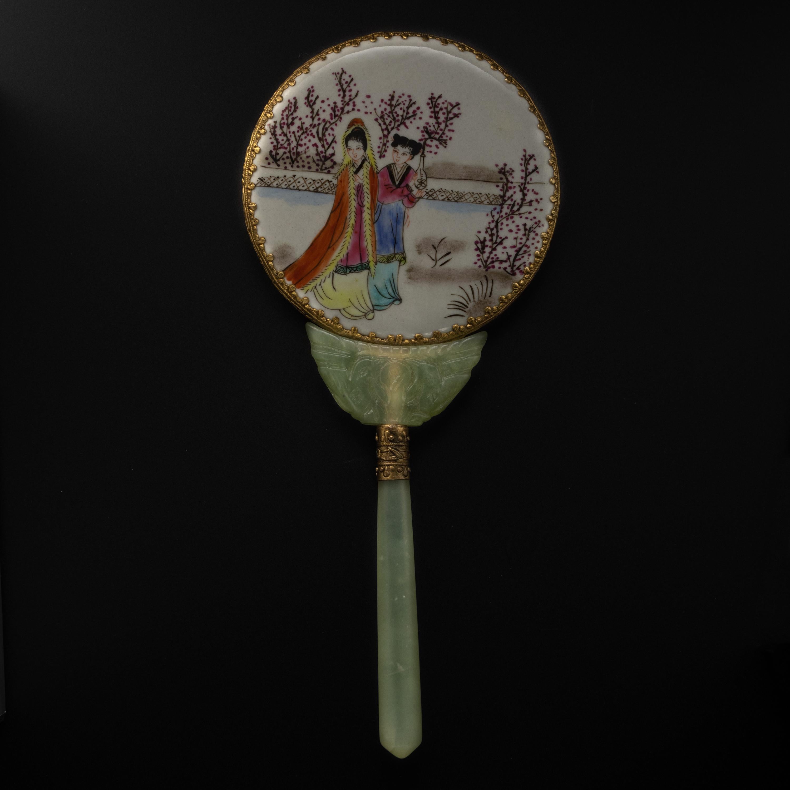 This circa 1910-1920 hand mirror is beautifully made from serpentine -a stone often mistaken for jade. The yellowish-green handle supports a fine porcelain backing which has been delicately hand-painted. The mirror is framed in ornate ormolu. The