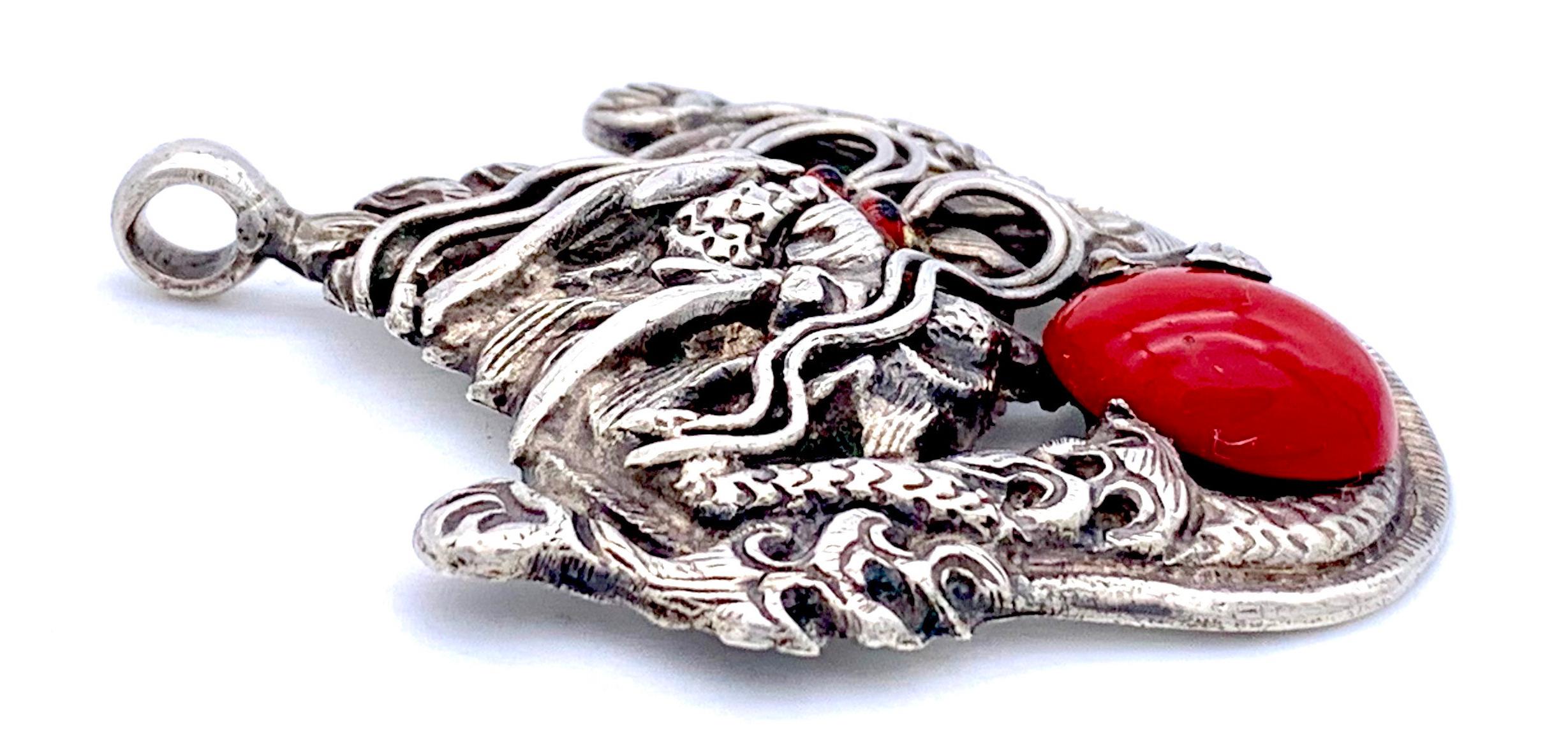 Ce pendentif chinois expressif en argent représente un dragon tenant dans ses griffes un cabochon en verre rouge. Les yeux des dragons sont faits de verre rouge et noir.
