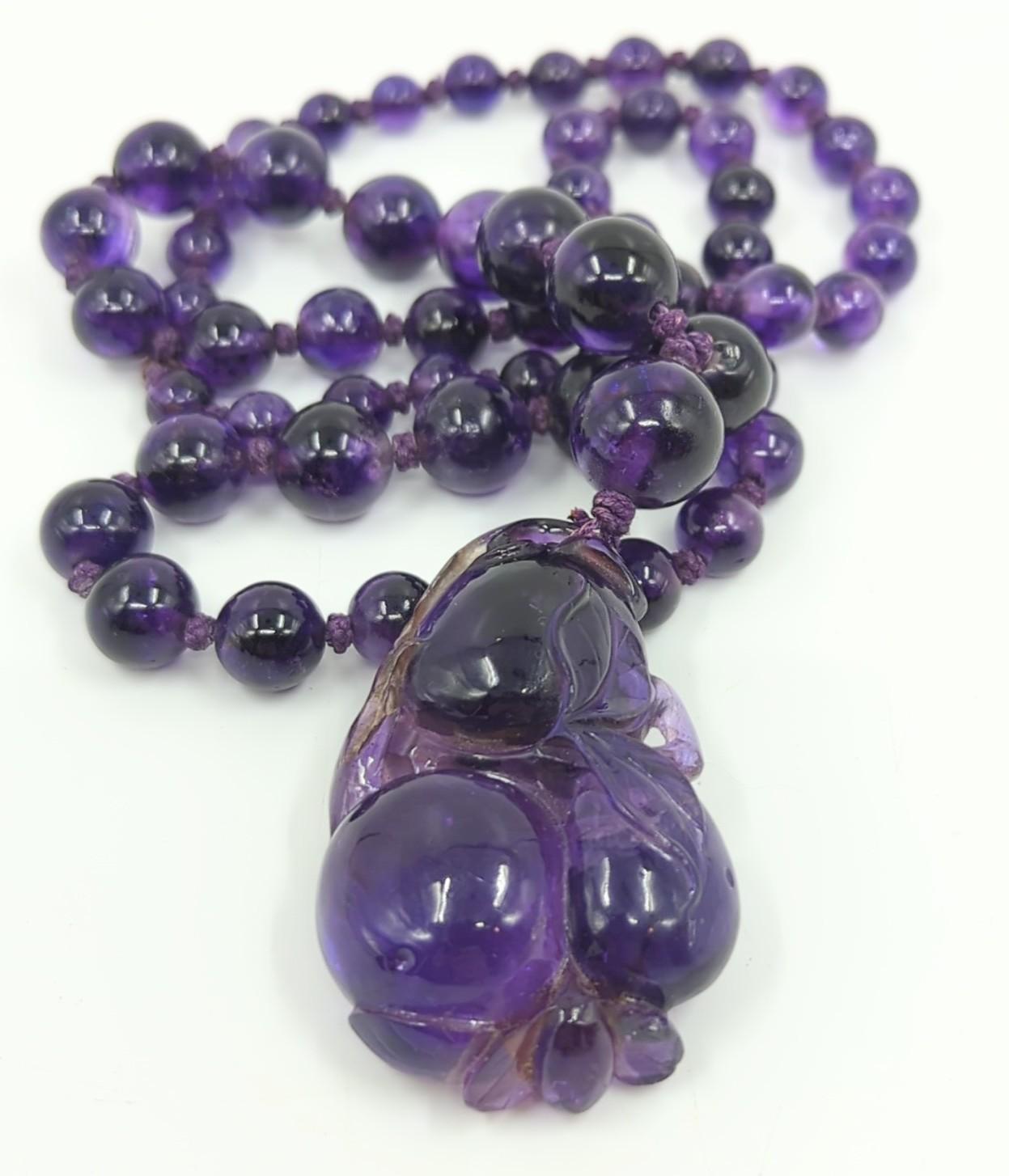 This late 19c to early 20c carved intense purple amethyst gemstone beaded necklace is comprised of a large, well carved amethyst double gourd pendant, and graduating amethyst beads from 7.0mm to 13.8mm in diameter. The necklace achieves a total