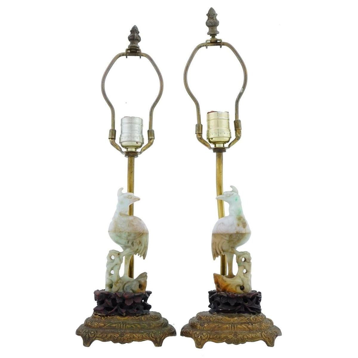 Pair of Chinese table lamps dating from the early 20th century featuring hand-carved jade figures of exotic standing birds mounted on carved rosewood bases and cast bronze stands.  With modern sockets and wiring, ready for use.