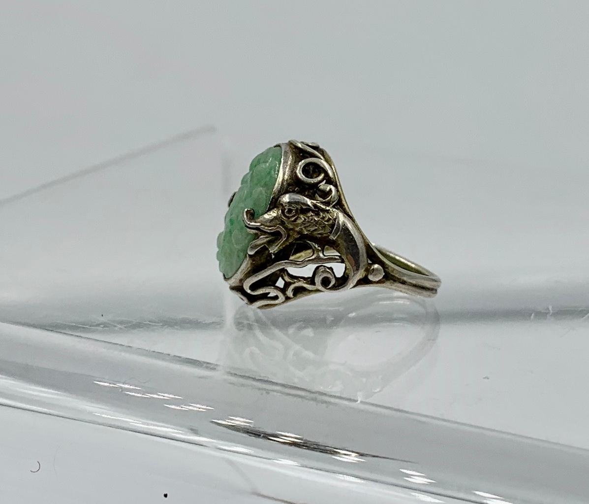 Dies ist ein wunderbarer und seltener Ring mit einer zentralen geschnitzten Jade in einem Blumenmotiv.  Die silberne Fassung für die Jade ist außergewöhnlich und zeigt ein fantastisches Drachenmotiv.  Die Drachen befinden sich auf beiden Seiten der