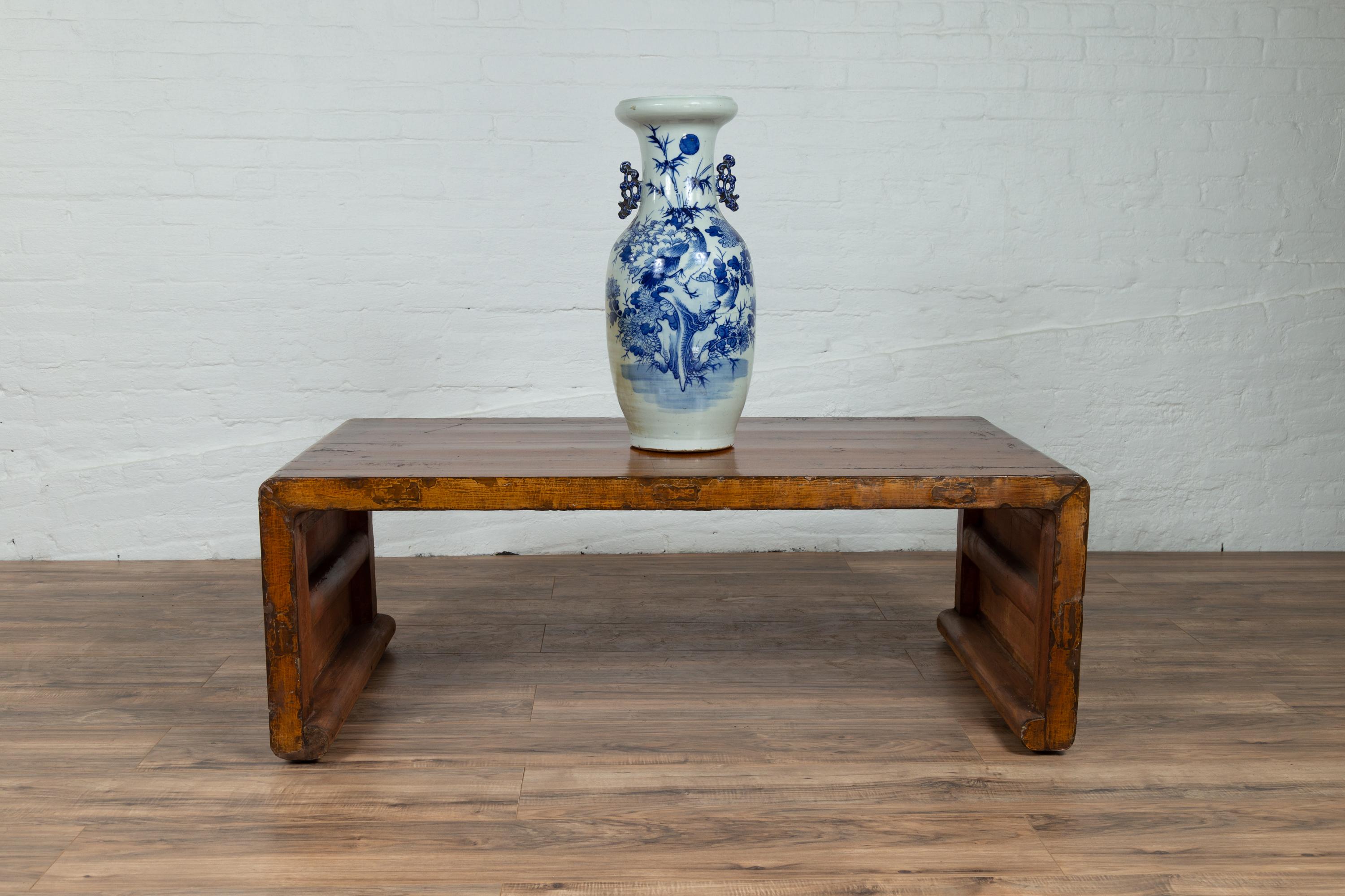 A Chinese antique waterfall coffee table from the early 20th century, with lacquered patina and scroll terminations. Found in Southern China, this waterfall table features a rectangular top raised on solid board legs with scrolled accents. The grand