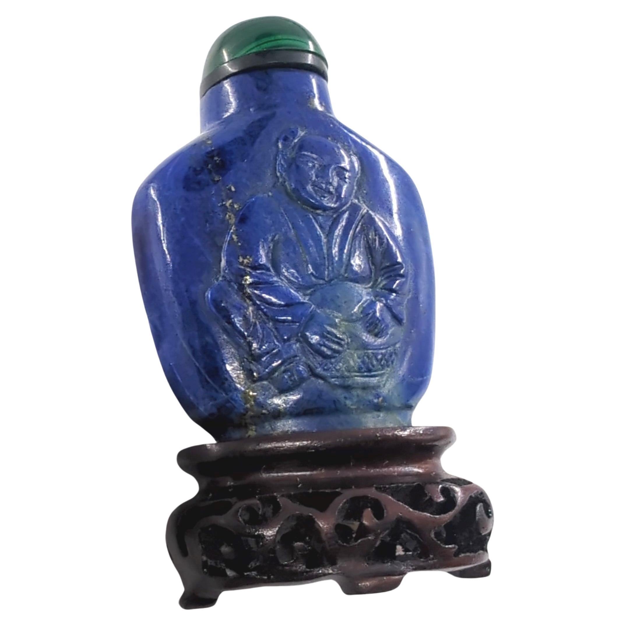 Antique Chinese hand carved lapis lazuli snuff bottle, relief carved with a boy figure to one side, and a flying bat to the other side, having a dished mouth and raised on a deep carved footring, with a green malachite stopper and a matching wood
