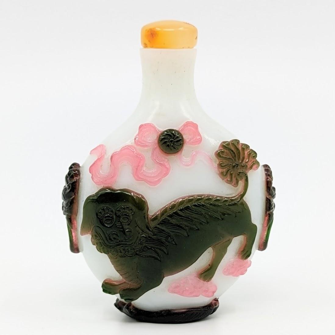 A very fine antique double color overlay glass snuff bottle, finely carved with a qilin gazing at books and a playful foo dog with a ball, among flowing pink ribbons and clouds, raised on double fish foot ring, with mask beast handles to shoulders,
