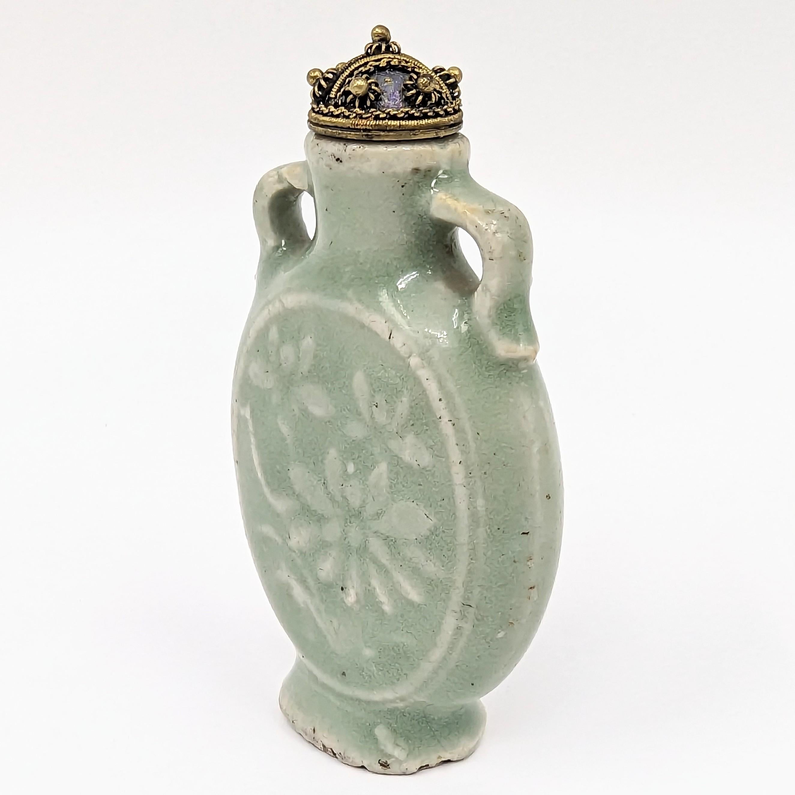 Antique Chinese Longquan celadon glazed porcelain snuff bottle with carved medallions of blooms and foliage in low relief, raised on a flared flat base, with stopper and spoon

19th Century, Qing Dynasty