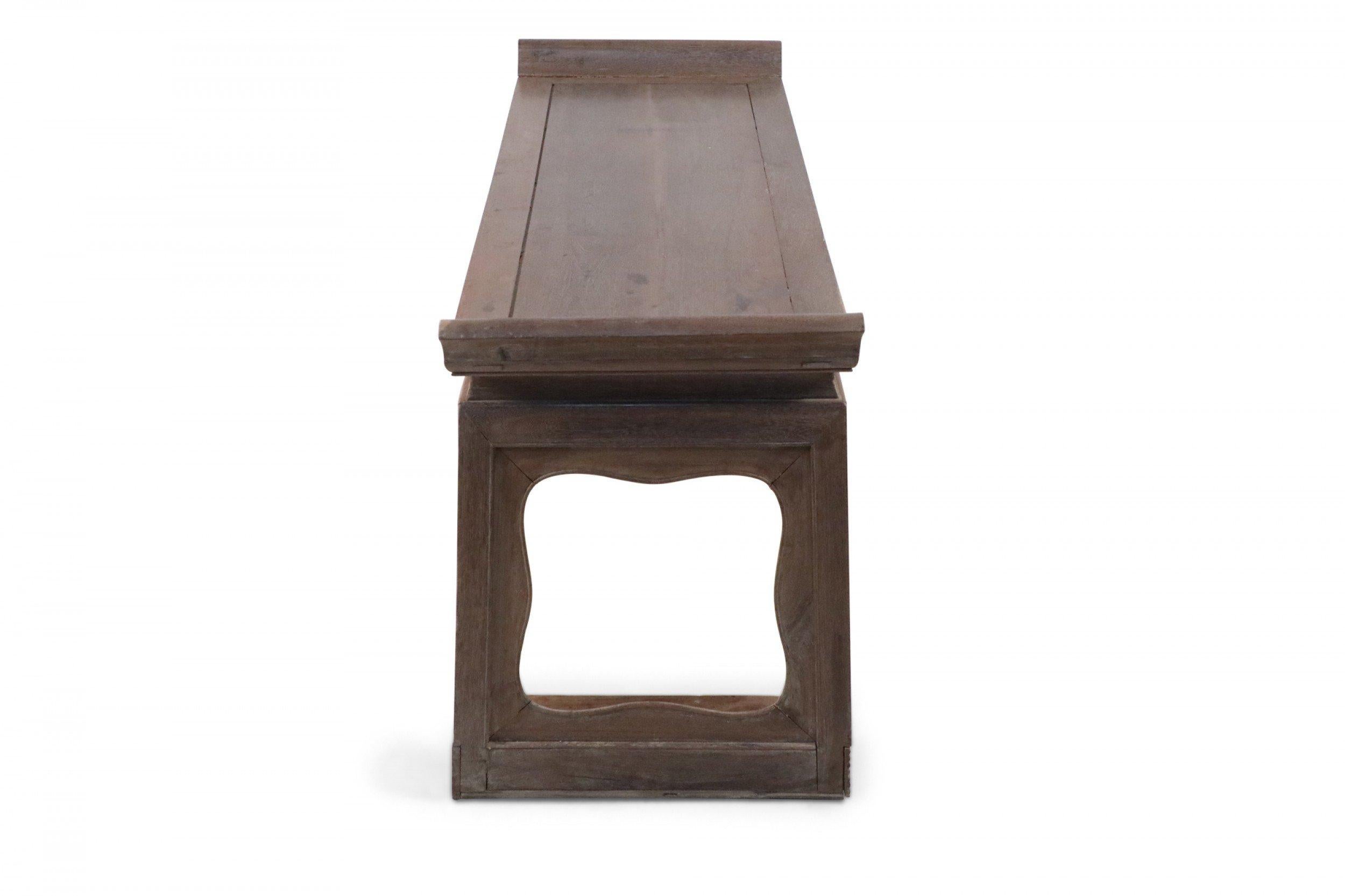 Antique Chinese (Early 19th Century) low narrow hardwood table or bench with a smooth, top slanting upward at each end, supported by two legs with subtly-scalloped cutouts.
