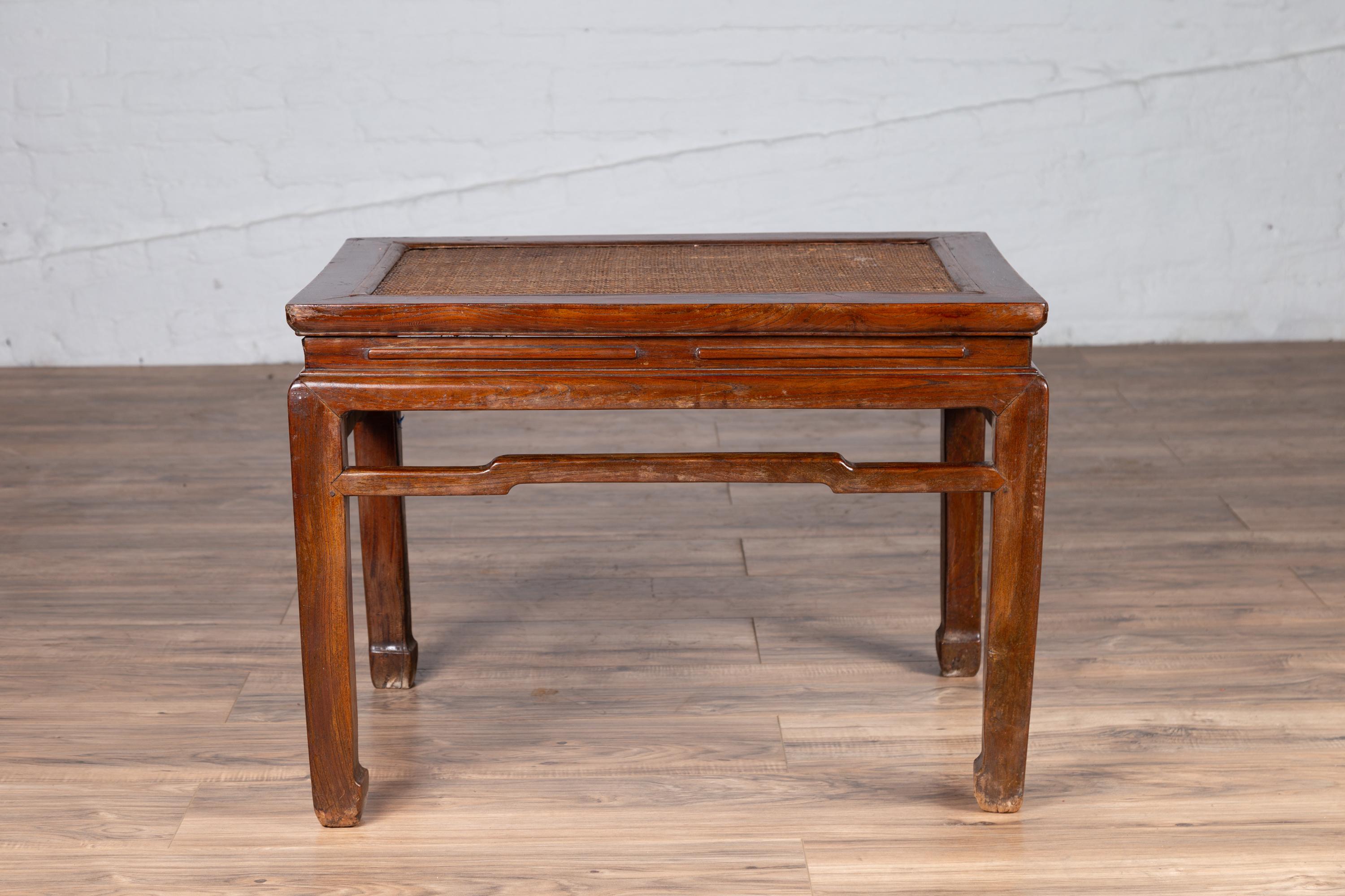 An antique Chinese Ming Dynasty style waisted side table from the early 20th century, with woven rattan top, humpbacked stretcher and horse hoof legs. Born in China during the early years of the 20th century, this elegant side table features a woven