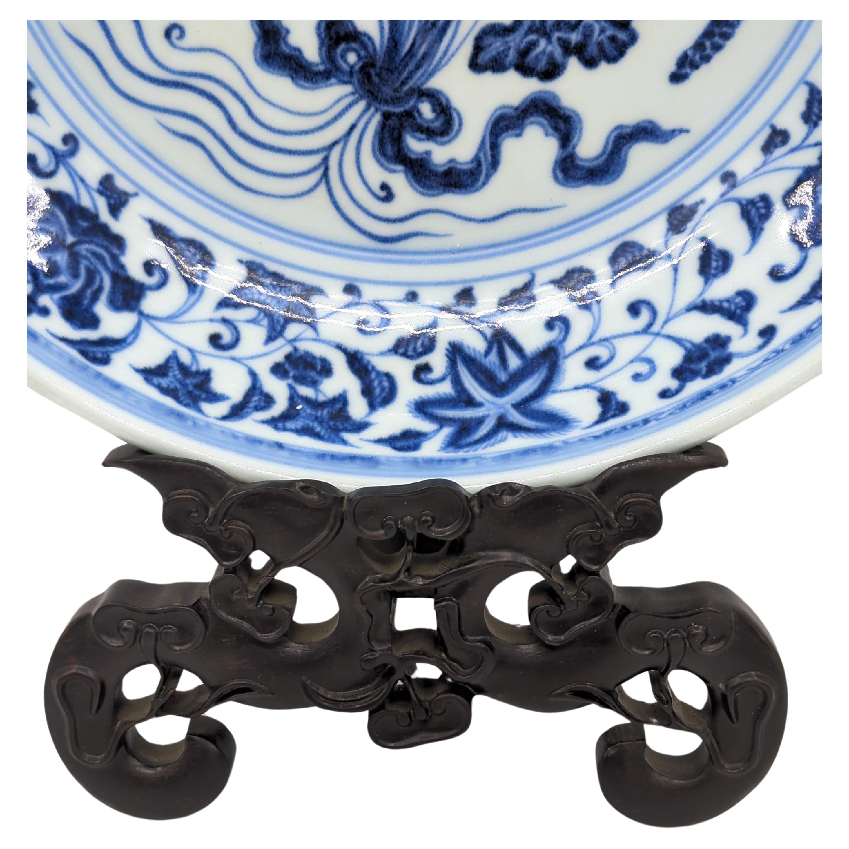 Chargeur ancien en porcelaine chinoise, décoré à la main en bleu et blanc sous glaçure, illustrant le style Revere Ming. Le point central, un médaillon à l'intérieur d'un double cercle, représente un bouquet de fleurs de lotus reliées par un ruban