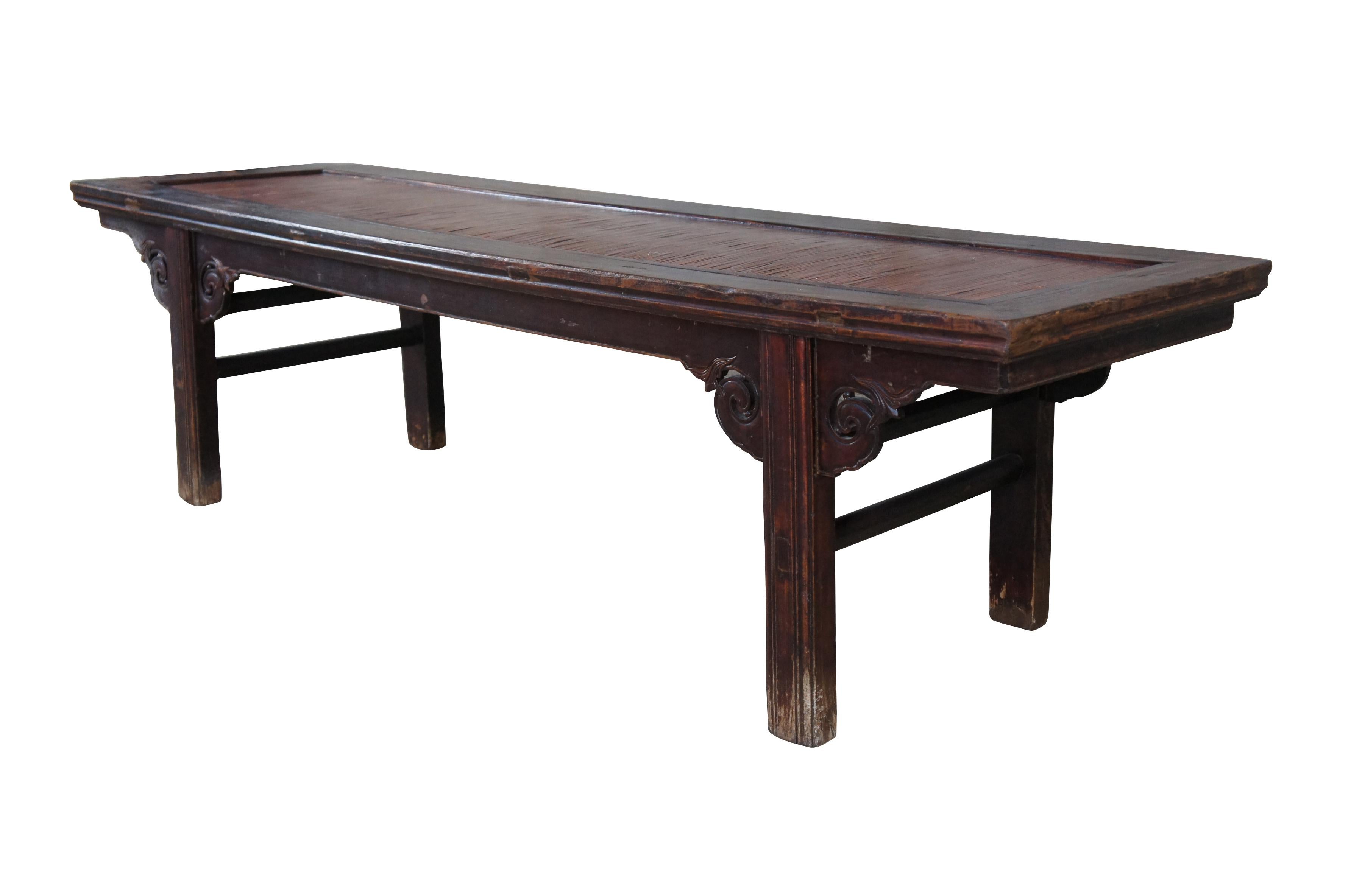 Charming late 19th century Chinese Qing Dynasty bench. Made from solid elm wood in mortise and tenon construction with an inset split reed top. Features cared and scrolled spandrals with foliate detail. Supported by straight legs connected by double