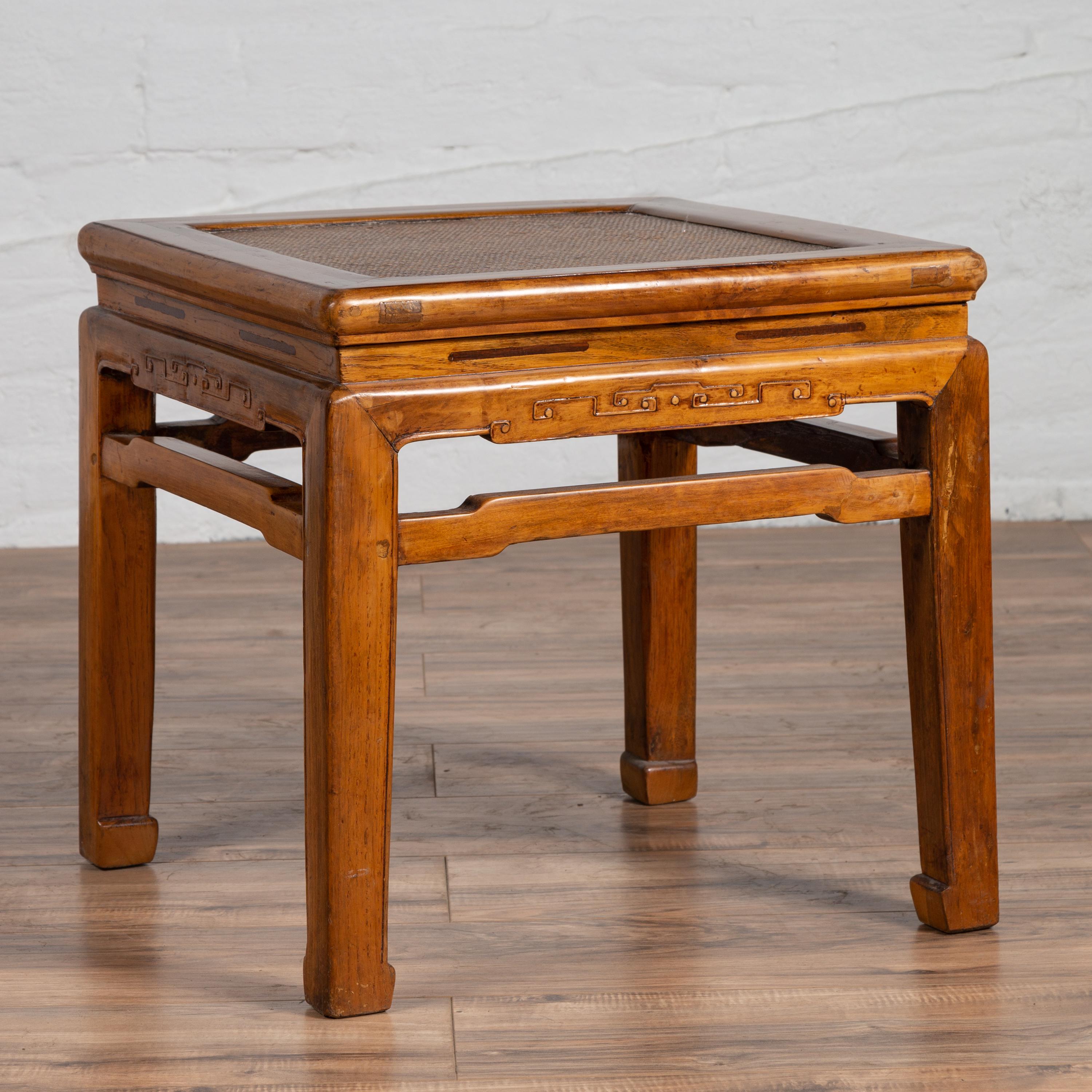 An antique Chinese Ming Dynasty style elmwood waisted side table from the early 20th century, with woven rattan top and horse hoof legs. Born in China during the early years of the 20th century, this elegant piece was originally conceived to be used