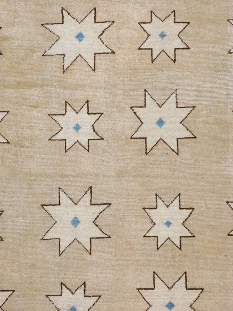 An antique Chinese Mongolian carpet from the early 20th century. Four columns of ivory stars of two distinct sizes decorate the grey-beige field which is framed by a cerulean blue border displaying disjoint knots. This carpet has a crisp, Art Deco
