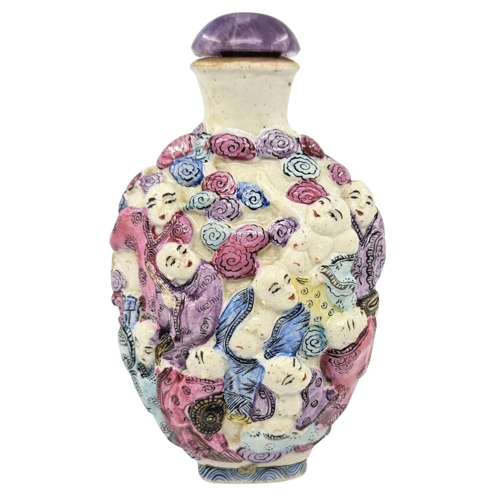 Antique Chinese moulded porcelain snuff bottle in compressed ovoid form, finely decorated in poly-chrome fencai with 18 Arhats Luohan in a continuous scene in high relief, with an outward flaring neck and mouth ring glazed in gold. Four character