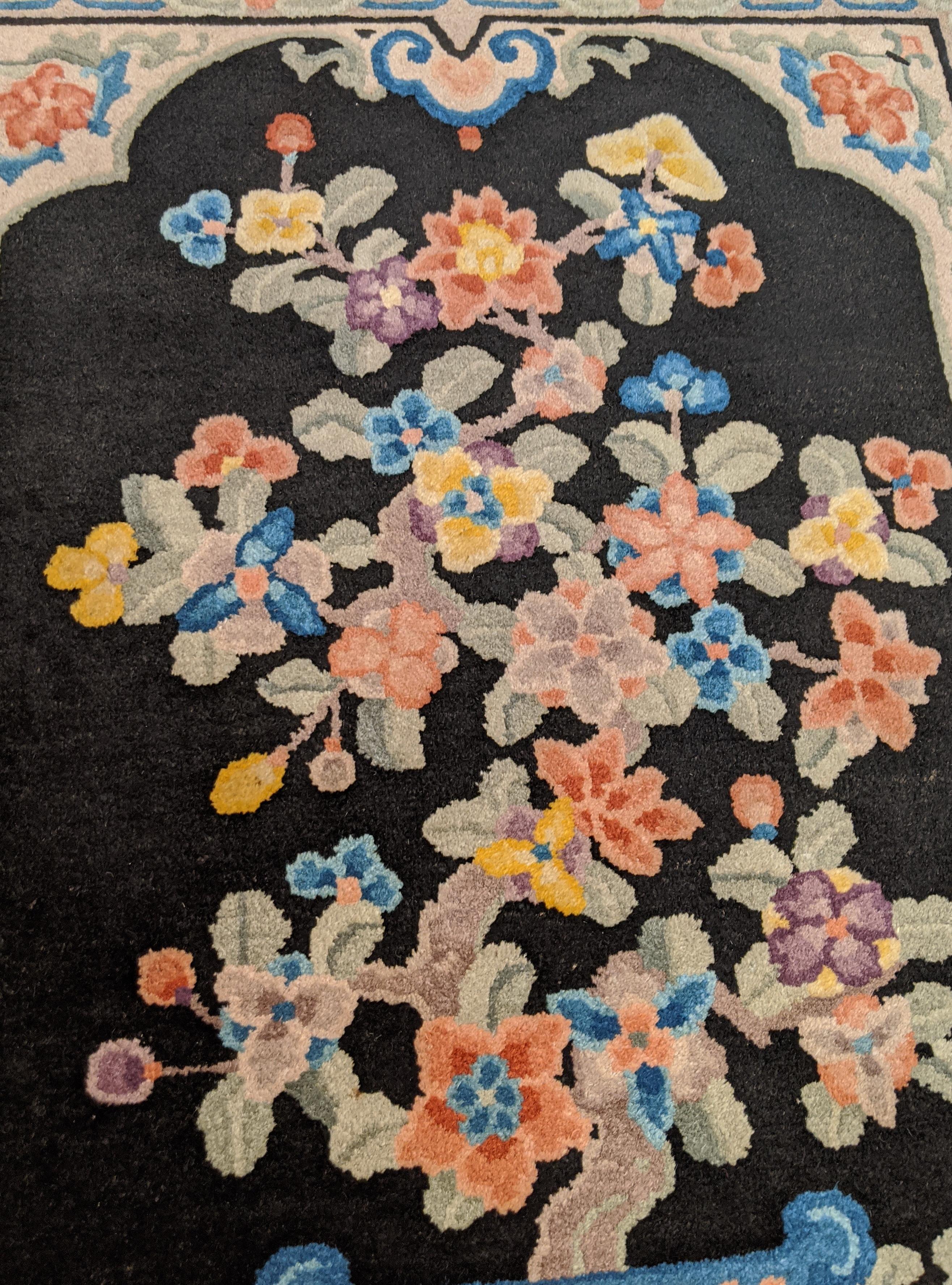 This is an antique Chinese known as a Nichols after the company that produced them in the early 20th century. These rugs are noted for their soft silky like wool and their traditional oriental motif. The black field is covered with a beautiful vase