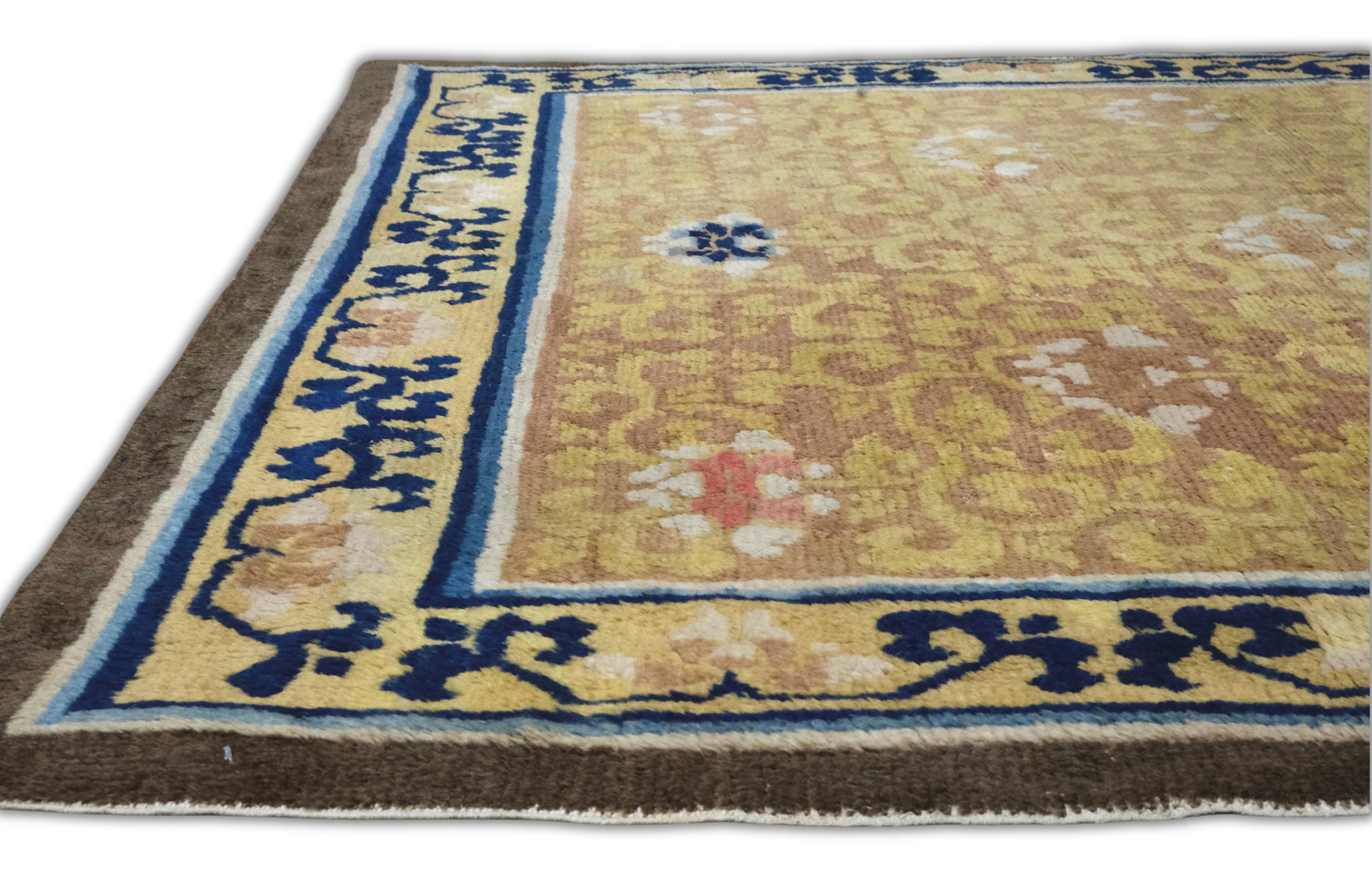 This antique Chinese Ningxia rug is a striking example of Qing-era artistry, showcasing a delicate interplay of traditional floral symbolism and Buddhist harmony. Hand-knotted in soft wool, the rug features a glowing golden-saffron field adorned