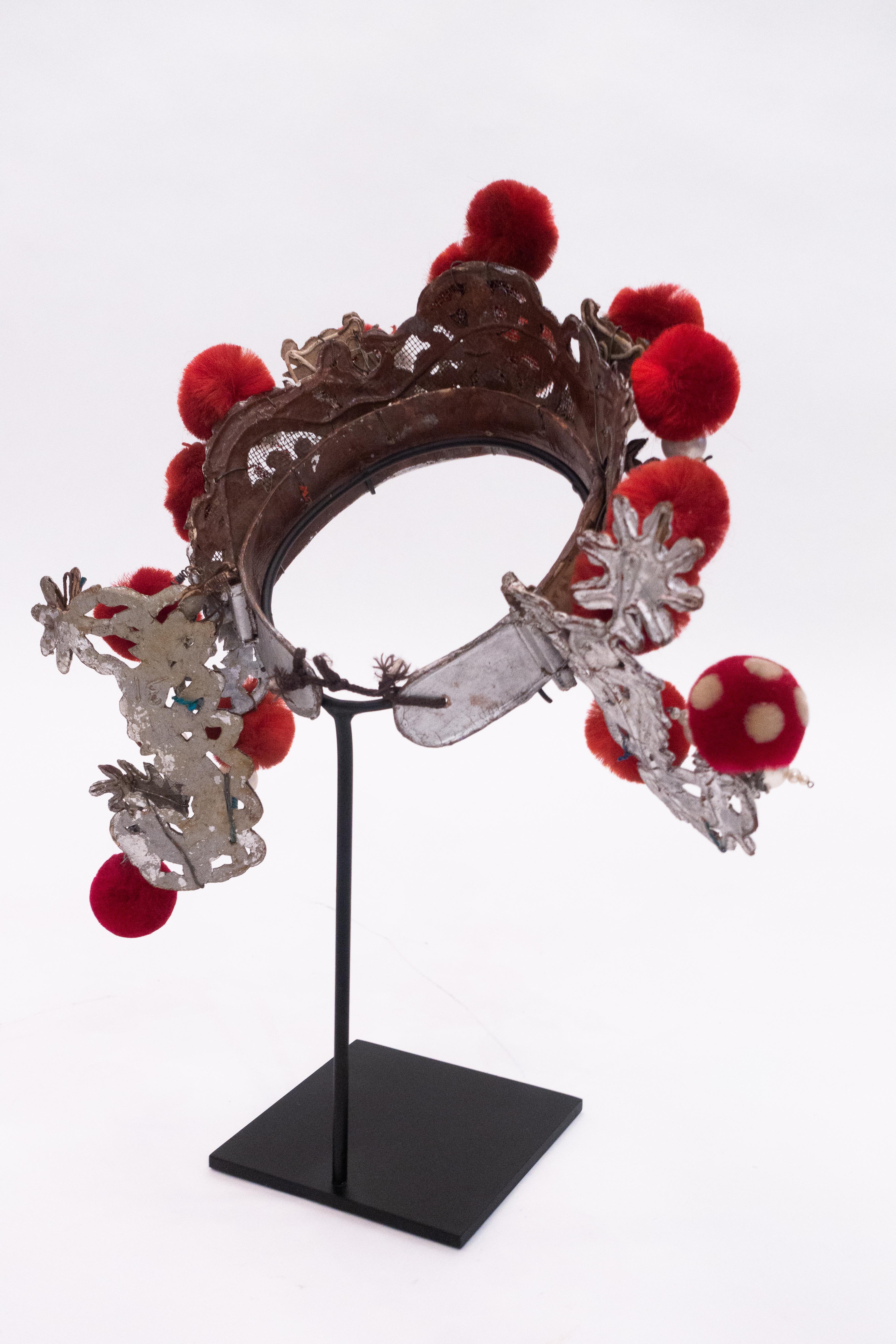 Chinese opera theatre headdress in turquoise papier mâché with red colored pom poms and faux pearls, early 20th century, mounted on a custom black painted metal base.