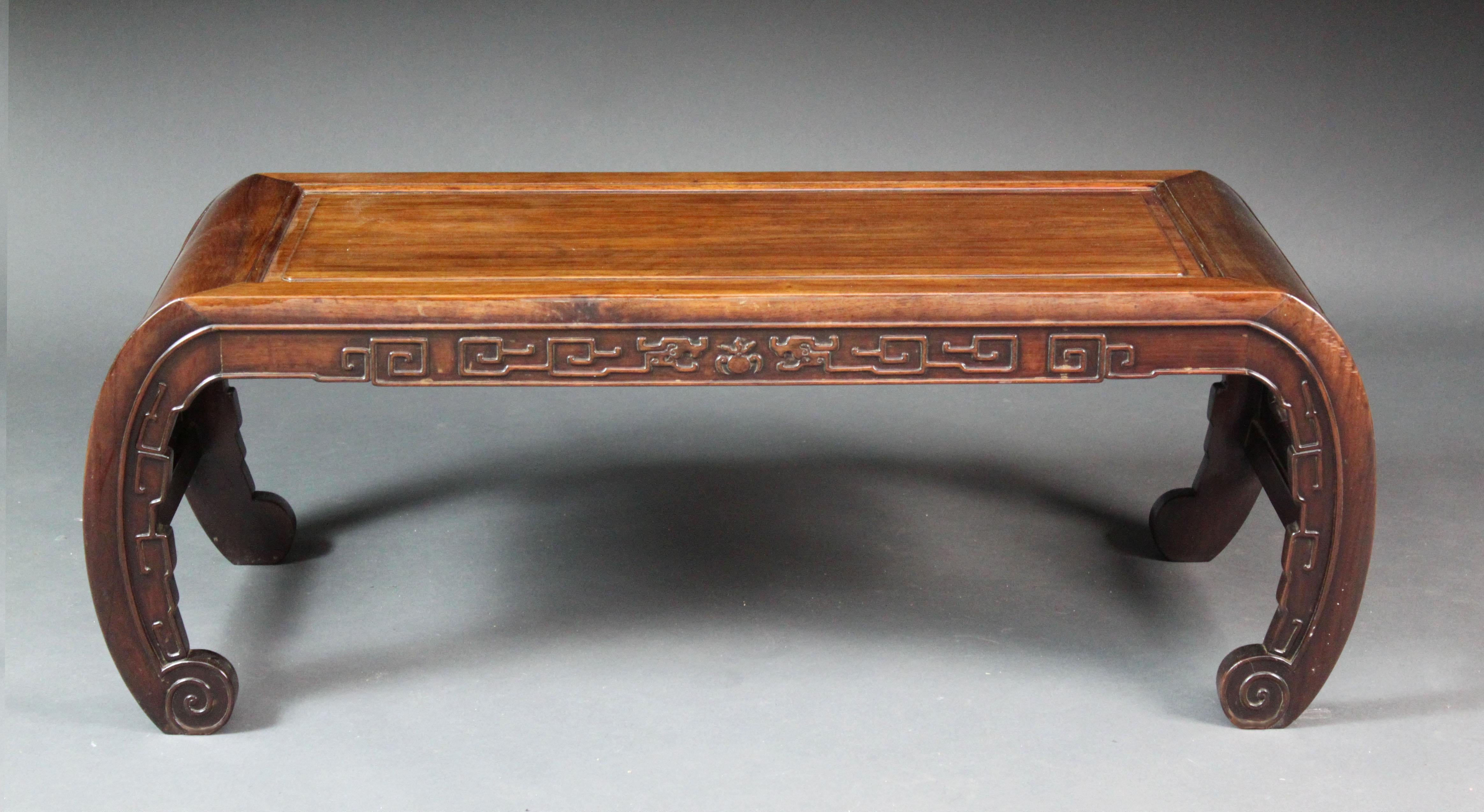 A late 19th/early 20th century Chinese hardwood low opium table with recessed panel top and carved bow ends; carved frieze on scrolled feet.

Top surface area 34.5