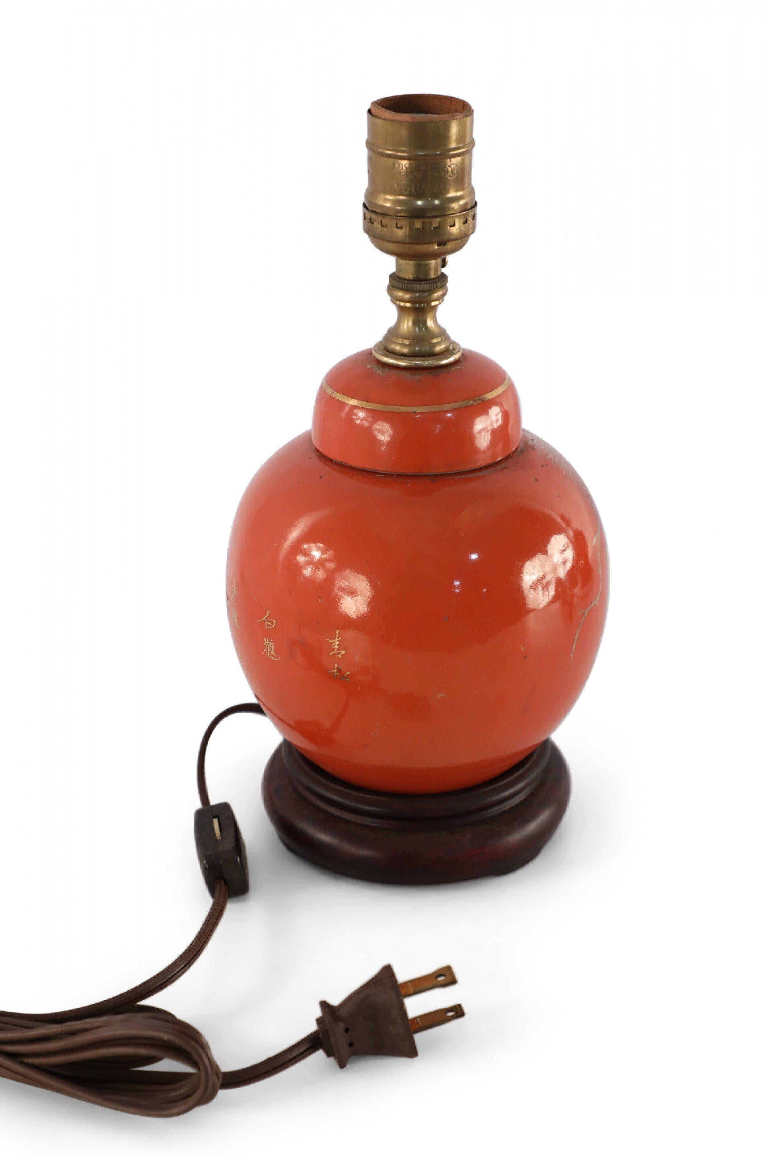 Antique Chinese (Early 20th Century) table lamp made from a round, orange, luster porcelain, lidded vase decorated with a gold crane design on one side and characters on the reverse, mounted on a wooden base and fitted with patinated brass