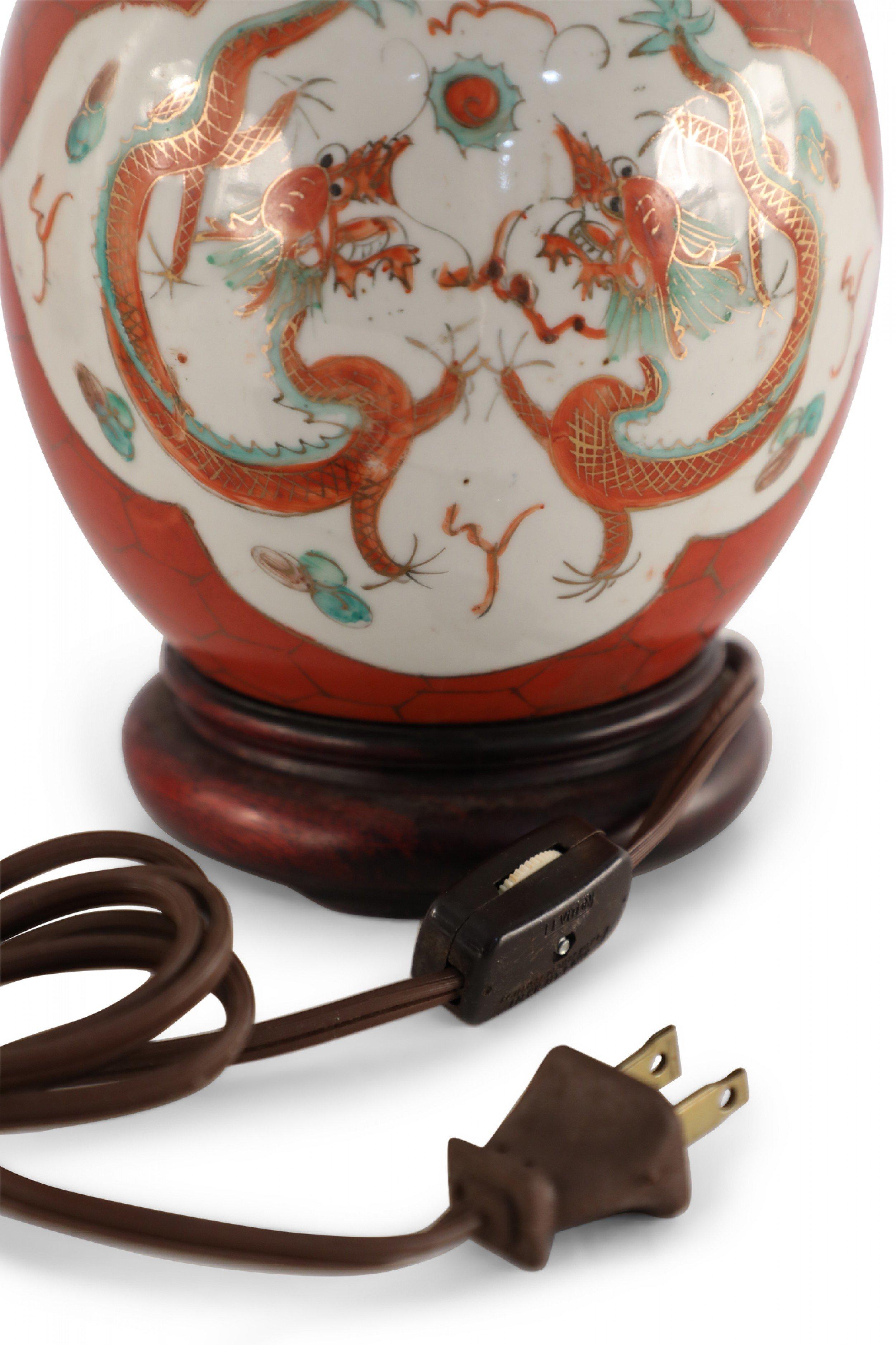 Antique Chinese (Early 20th Century) table lamp made from a round, luster porcelain vase with an orange and gold hexagonal patterned ground against two white cartouches depicting dragons, mounted on a wooden base with brass hardware.
 