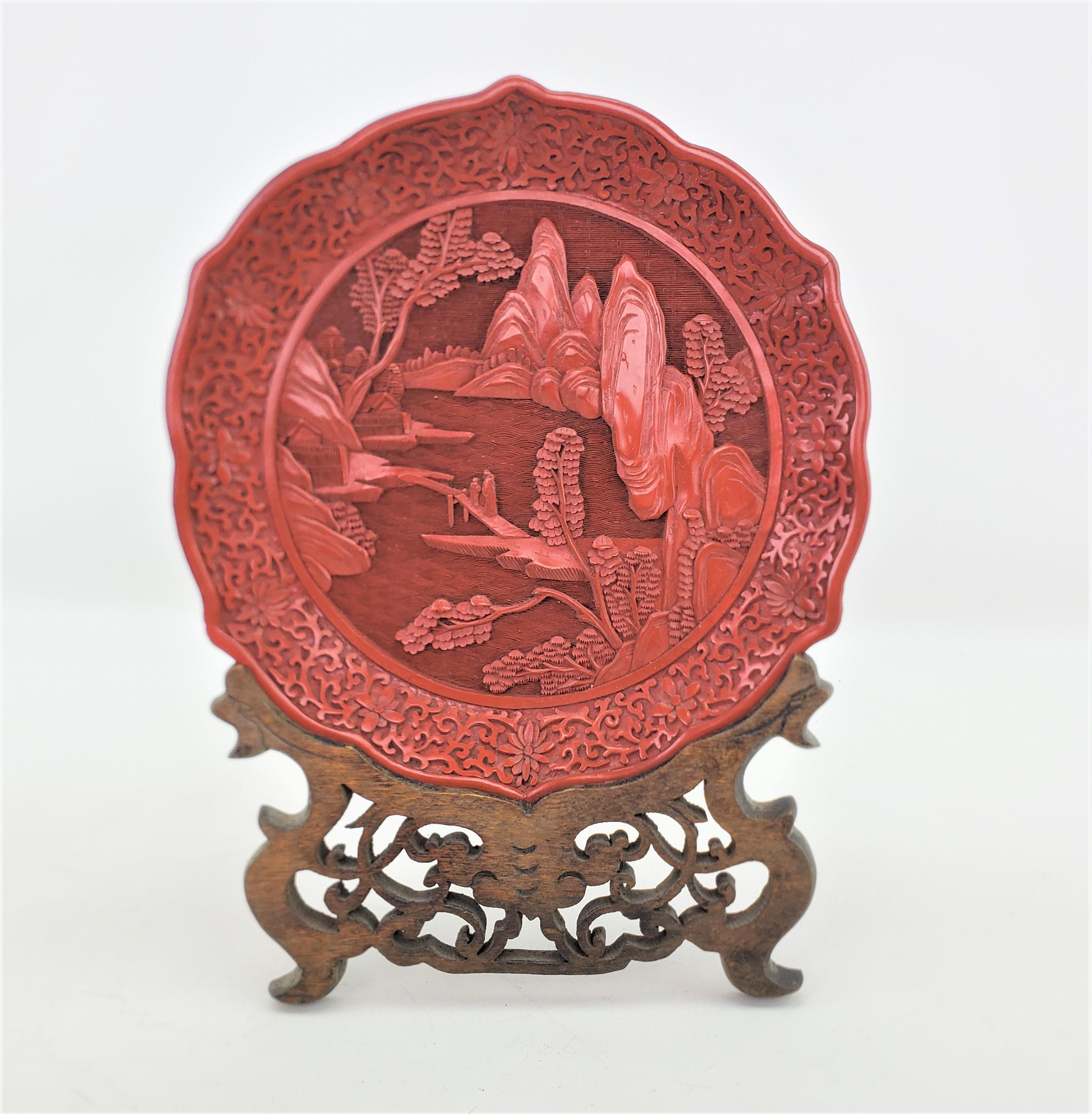 This antique carved plate is unsigned, but presumed to have originated from China and date to approximately 1920 and done in a Chinese Export style. The plate is composed of cinnabar and is ornately carved with a mountain landscape scene with