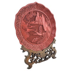 Ancienne assiette Cinnabar chinoise sculptée de façon ornementale avec scène de paysage et support en bois