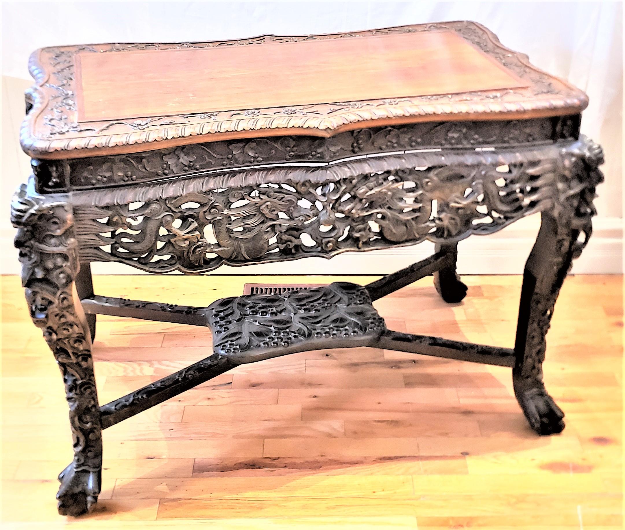 This antique very ornately carved hardwood writing or accent table is unsigned, but presumed to originate from China and date to approximately 1890 and done in the period Qing style. The table is composed of elm with a serpentine curved top with a