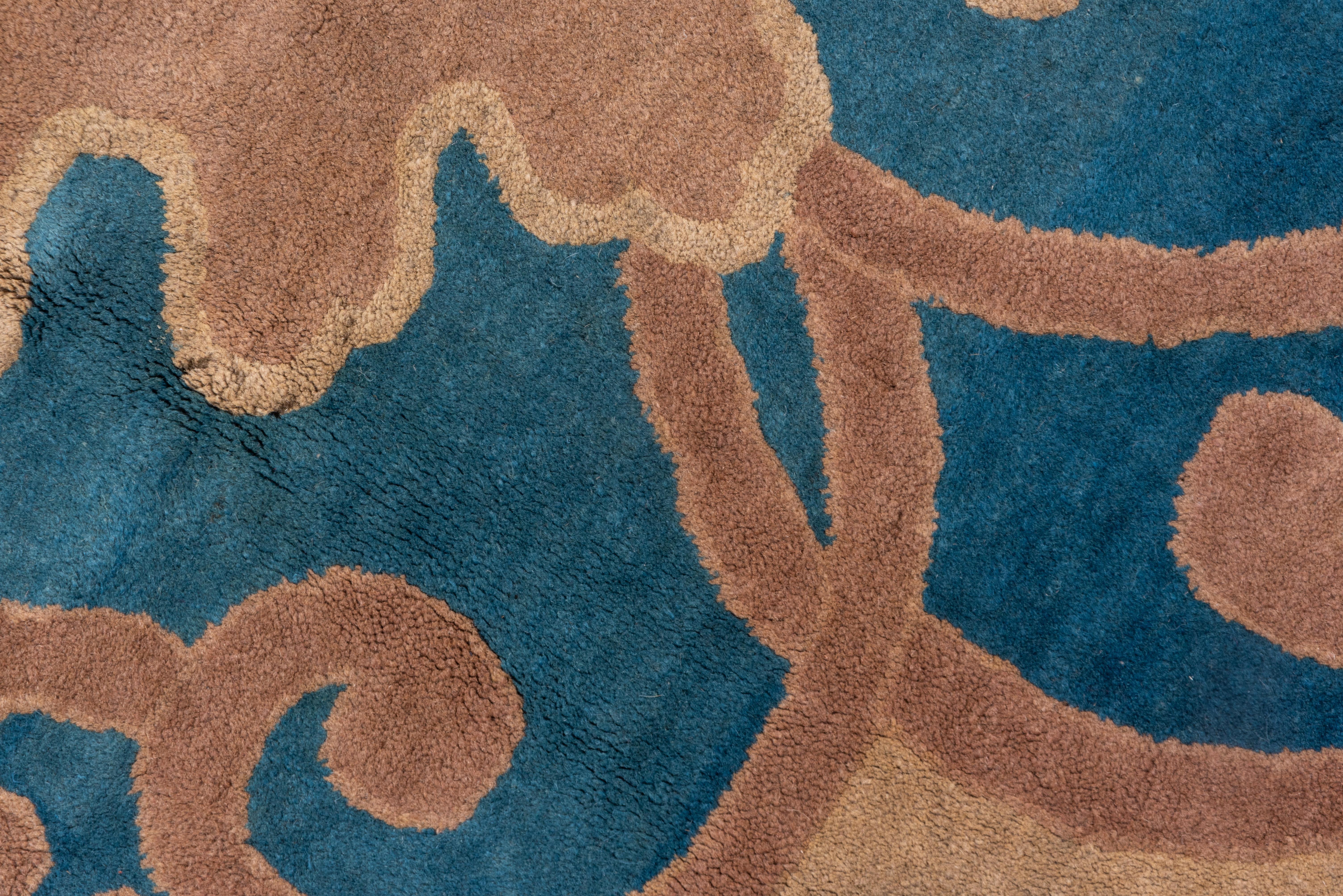 This European-style Peking carpet shows a central tan, lappet-edge medallion with internal strapwork arabesques, on the light blue ground. Five petal rosettes appear in the sandy beige main border which has a volute inner edge. The plain blue outer