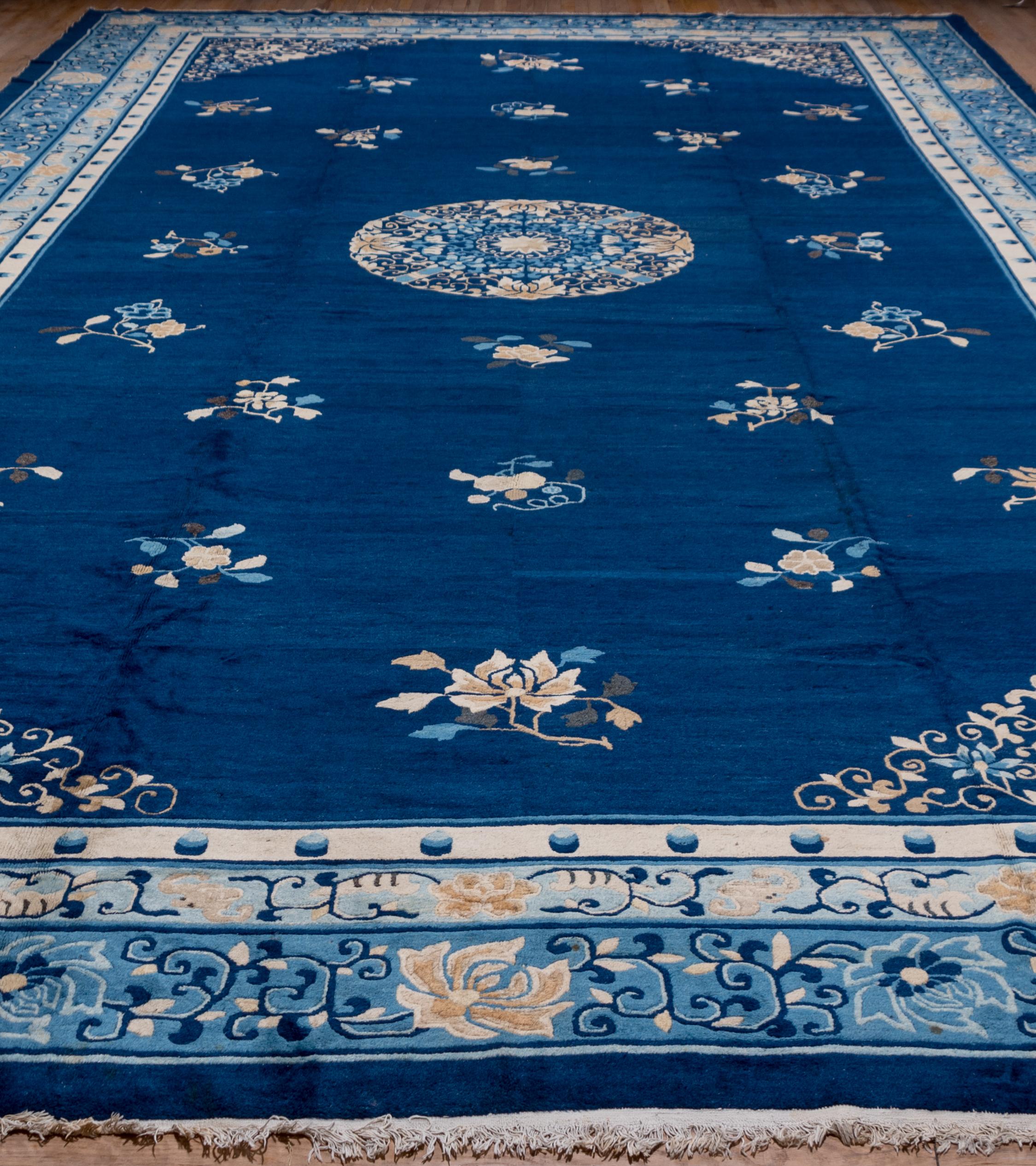 This blue and white Classic Peking workshop carpet has a round floriate medallion, sprays of seasonal flowers and filigree corners with cloud ribbons. The field is a rich deep blue and there are at least three other blues including a light blue in