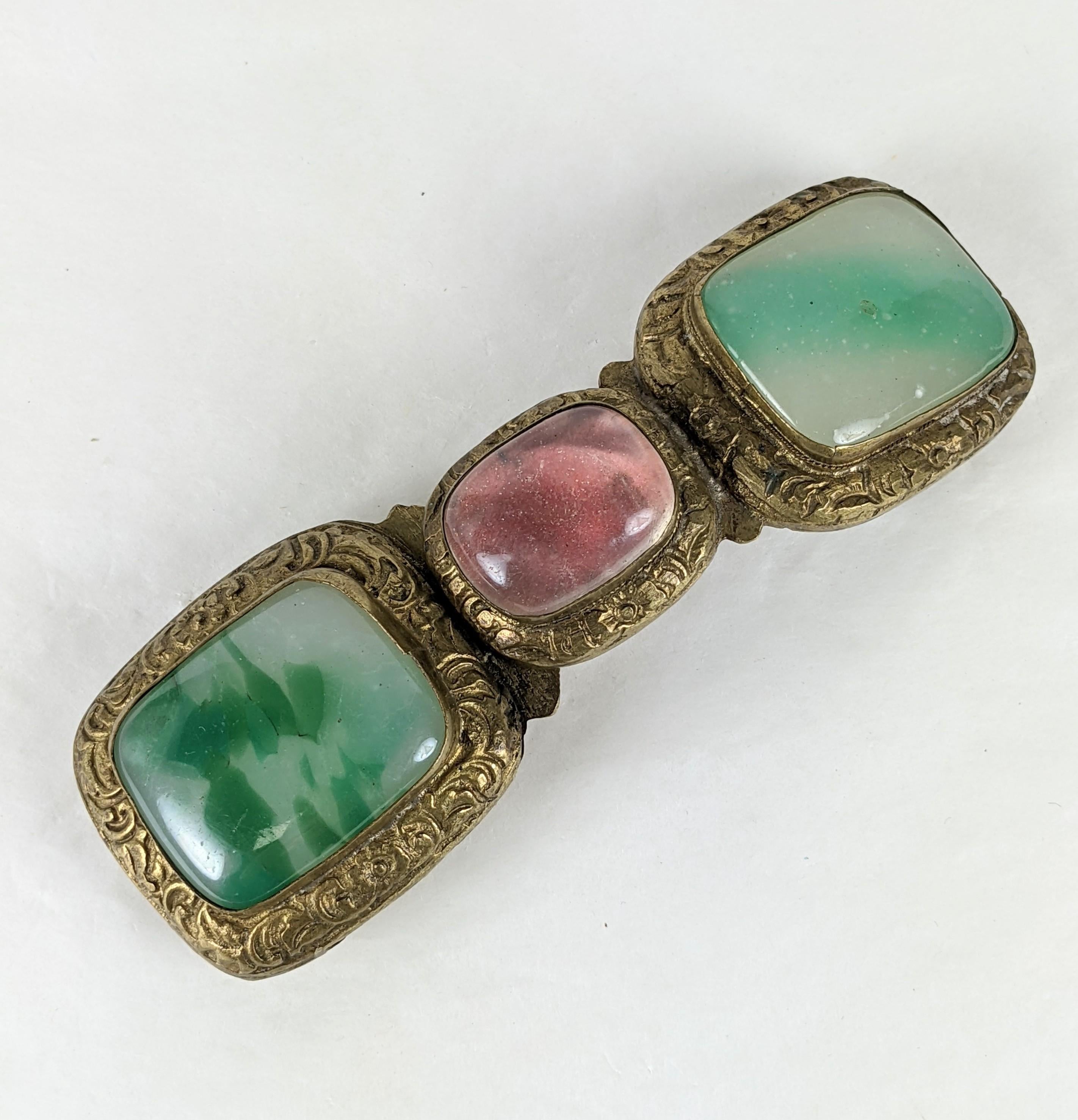 Antique Chinese Peking Glass Buckle from the late 19th Century. Set in incised bronze with decorative scrolled border and floral patterned back. Peking glass is used to replicate jade and an oval cabochon is set over pinkish red paper/textile to