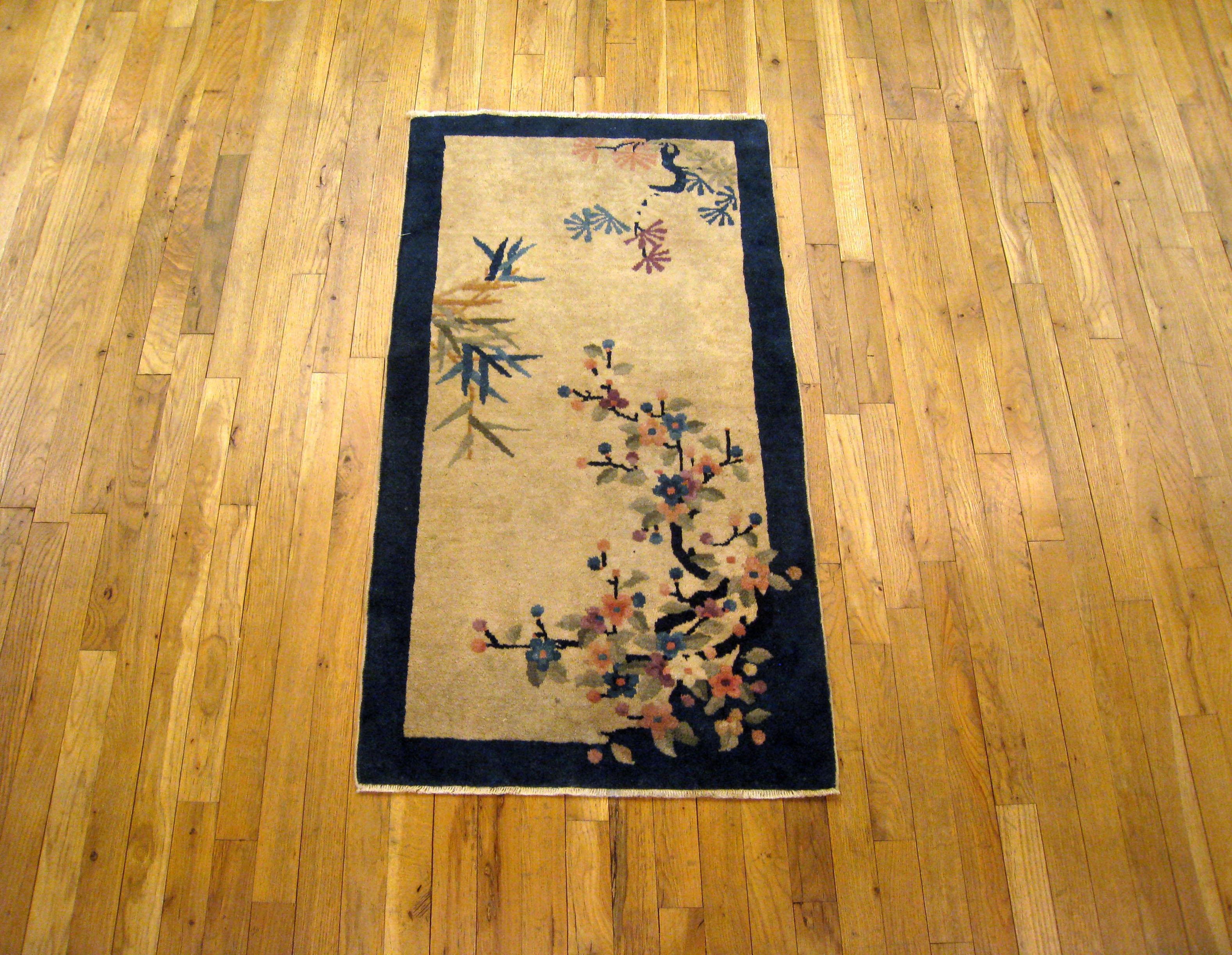 An antique Chinese Peking oriental rug, size 4'0 x 2'2, circa 1900. This lovely hand-knotted oriental carpet features an uncluttered central field characterized by decentralized flower and tree motifs on a soft background, enclosed within a navy