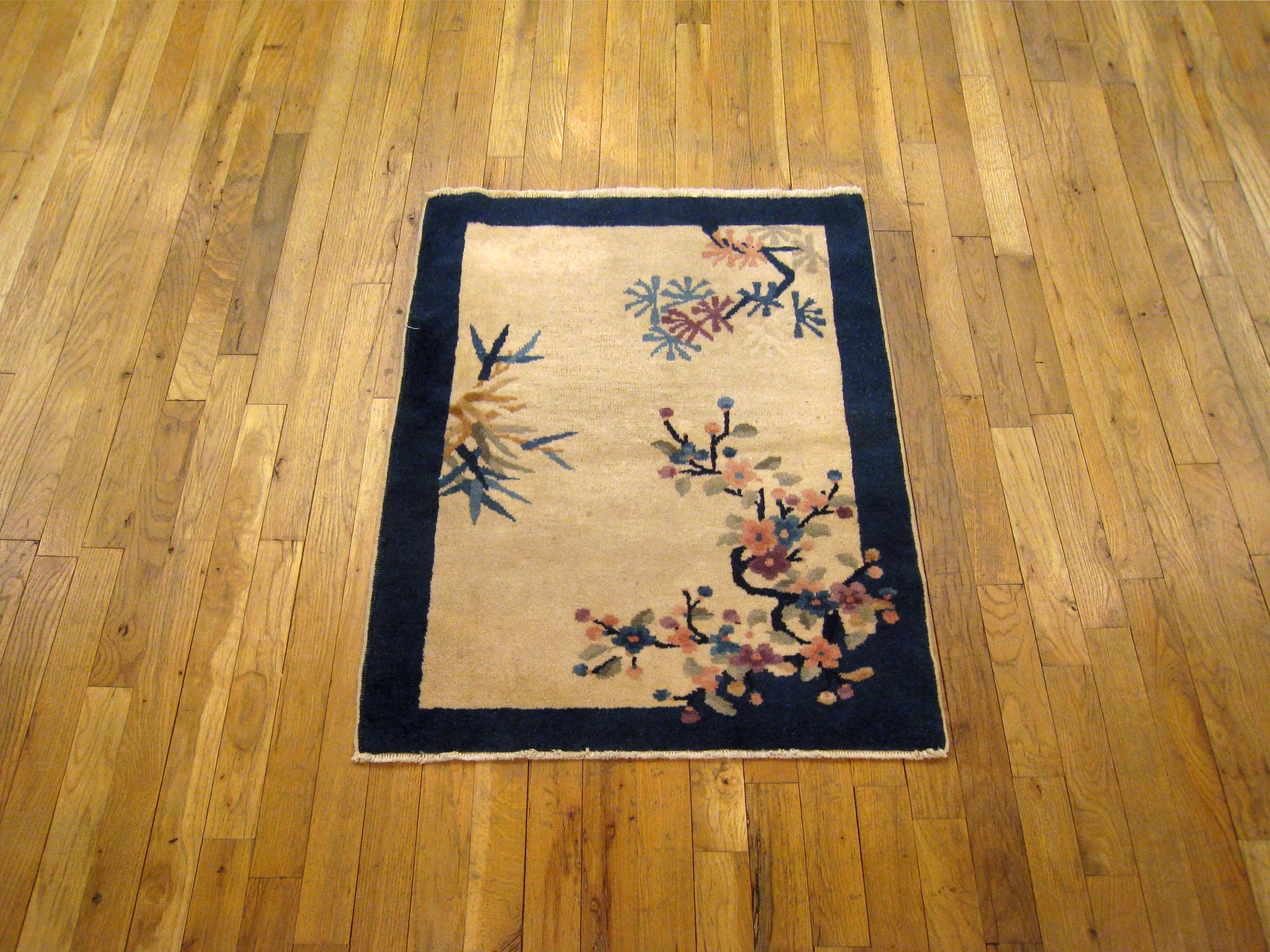 An antique Chinese Peking oriental rug, size 3'0 x 2'2, circa 1900. This lovely hand-knotted oriental carpet features an uncluttered central field characterized by decentralized flower and tree motifs on a soft background, enclosed within a navy