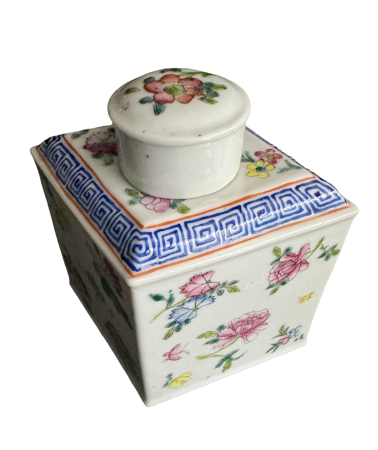 A gorgeous early 20th century footed porcelain tea caddy in the shape of a diamond. The top on caddy with a Greek key design in a deep blue. The body is hand painted with pink, yellow and blue florals with various shades of green foliage. A matching