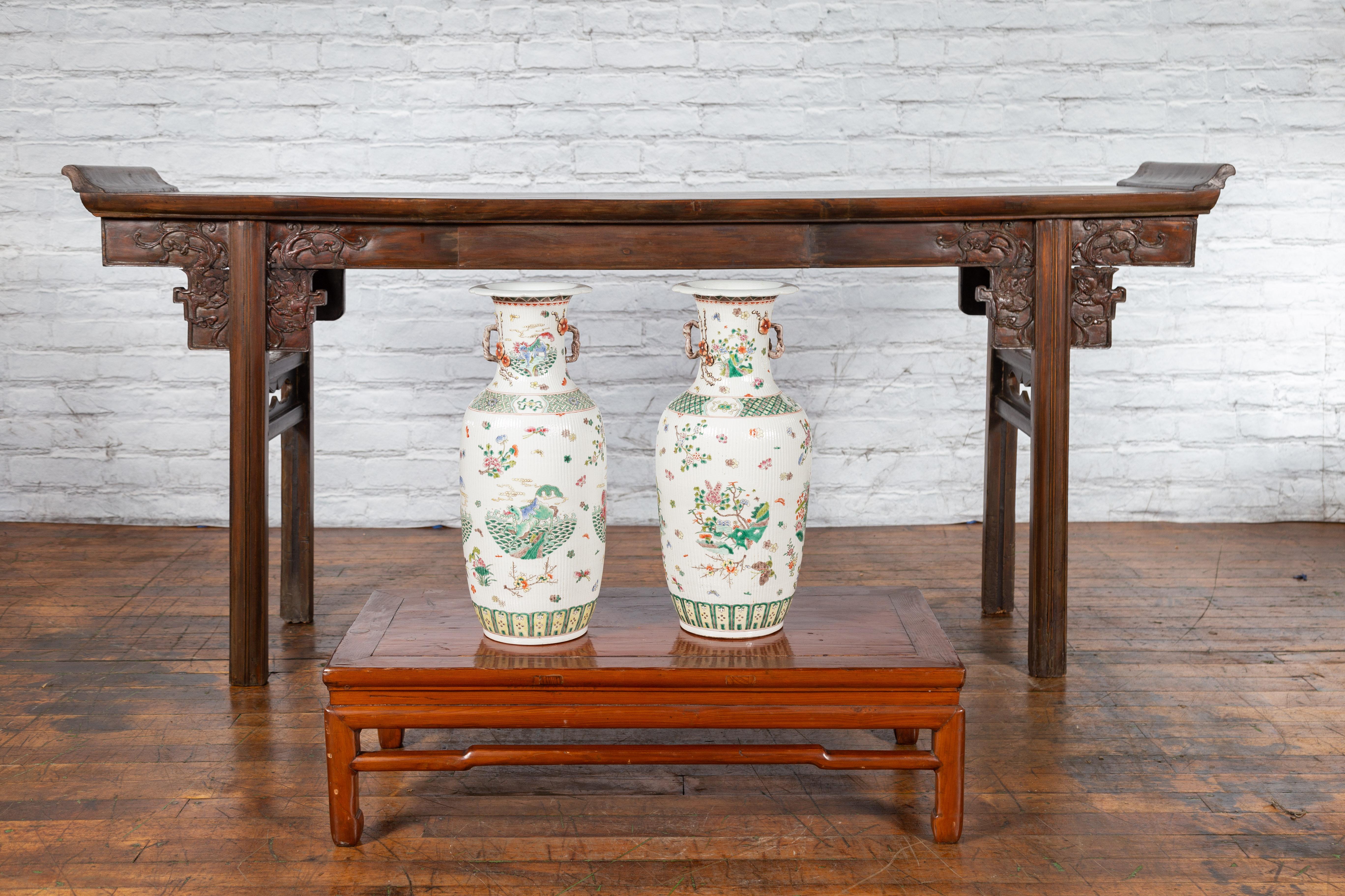 A pair of Chinese antique porcelain vases from the early 20th century, with hand-painted flowers, butterflies and mythical animals. Created in China during the early years of the 20th century, each of this pair of porcelain vases attracts our