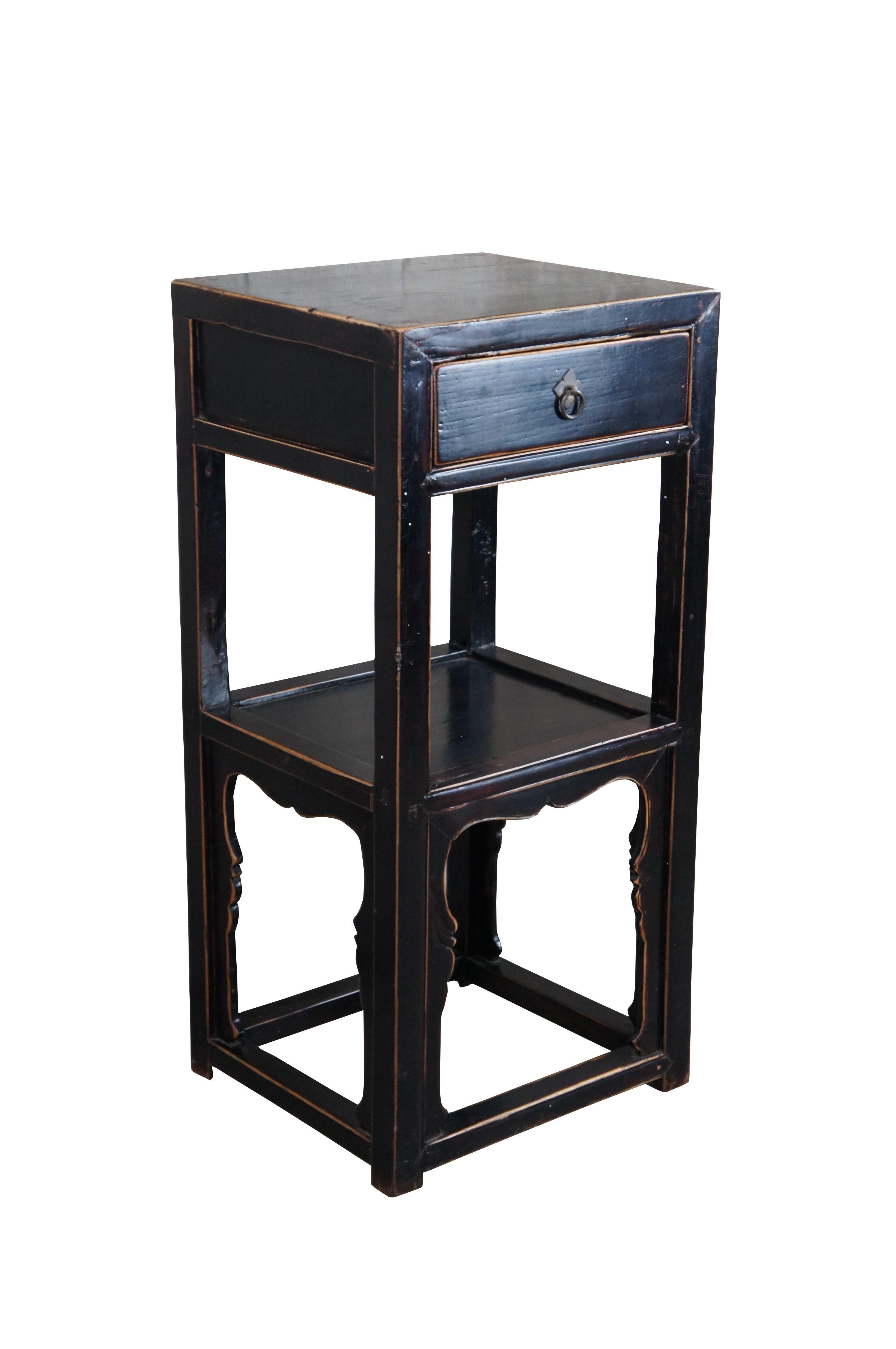 Late 19th Century Chinese Qing Dynasty Tiered Side Table or Sculpture Pedestal / Plant Stand. Made from elm with a black lacquer finish. Features a dovetailed drawer, lower shelf and serpentine carved spandrels. Drawer has a brass pull with ring and
