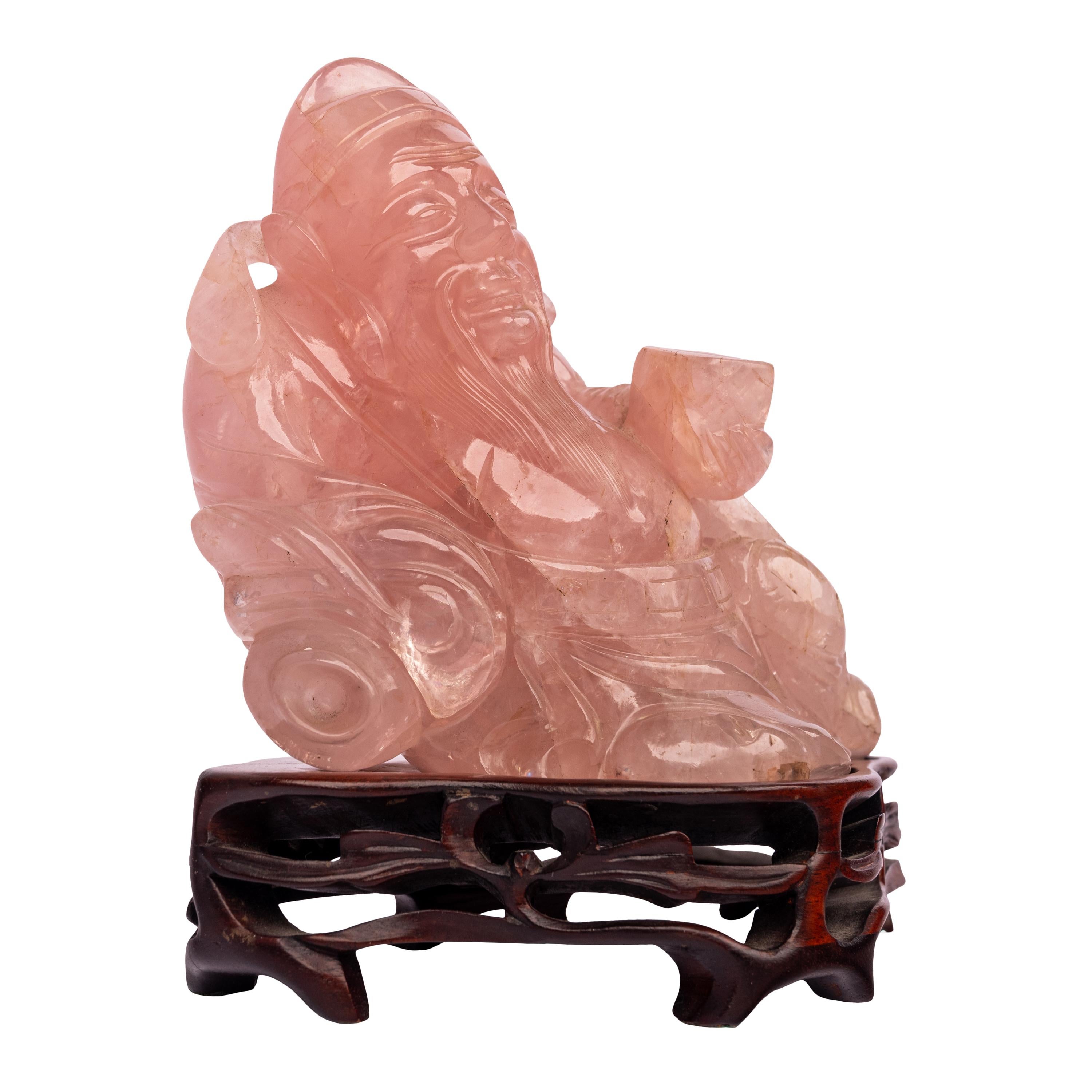 A good antique Chinese Qing dynasty carved rose quartz buddha/hotei figure on a carved rosewood stand, circa 1910.
The figure modeled as a buddhistic recumbent figure, the figure is finely carved from rose quartz and rests on a carved rosewood