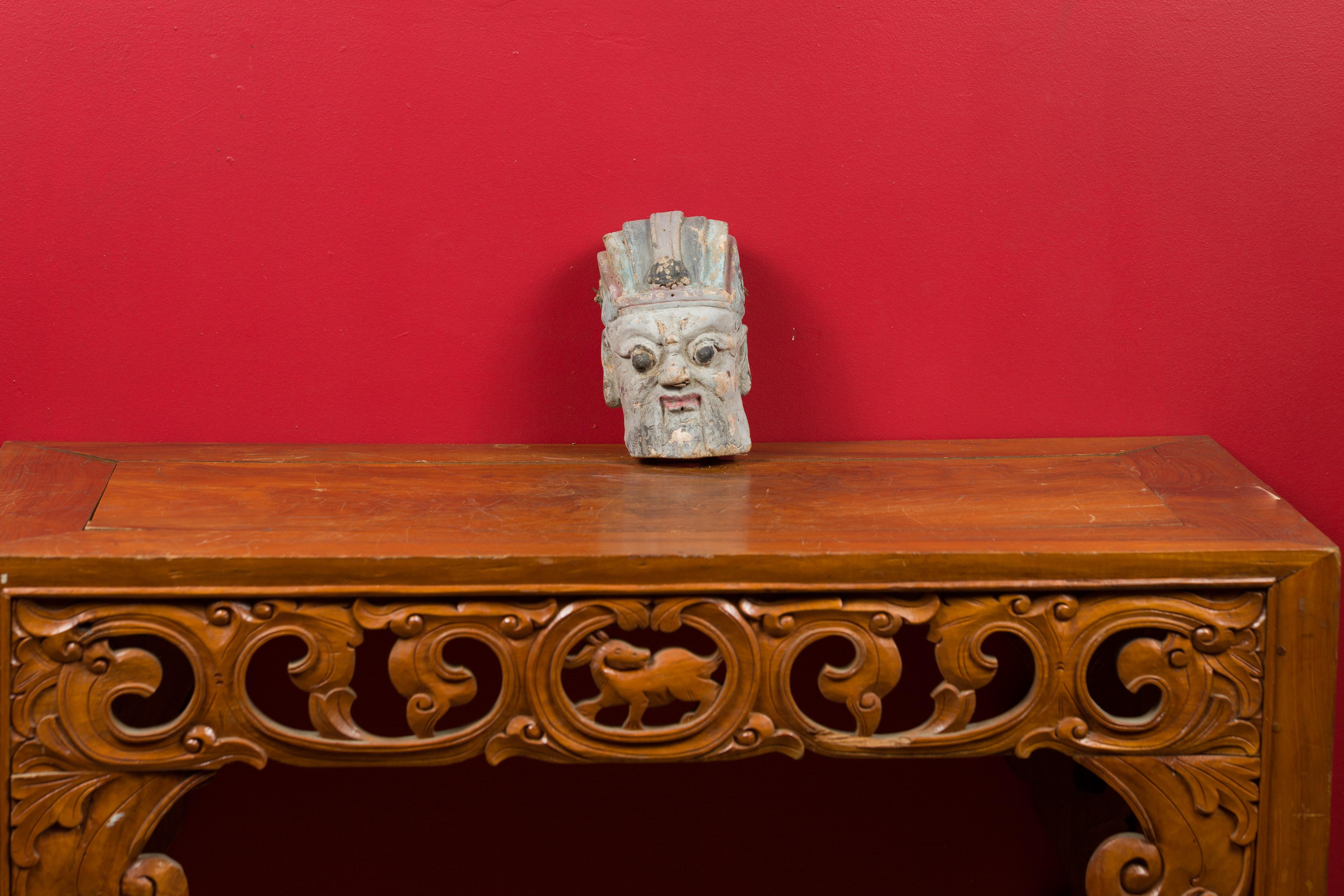 An antique Chinese Qing hand painted terracotta head from the 19th century, with striking features and headdress. Created in China during the Qing Dynasty, this painted terracotta head captures our attention with its soft colors and nicely