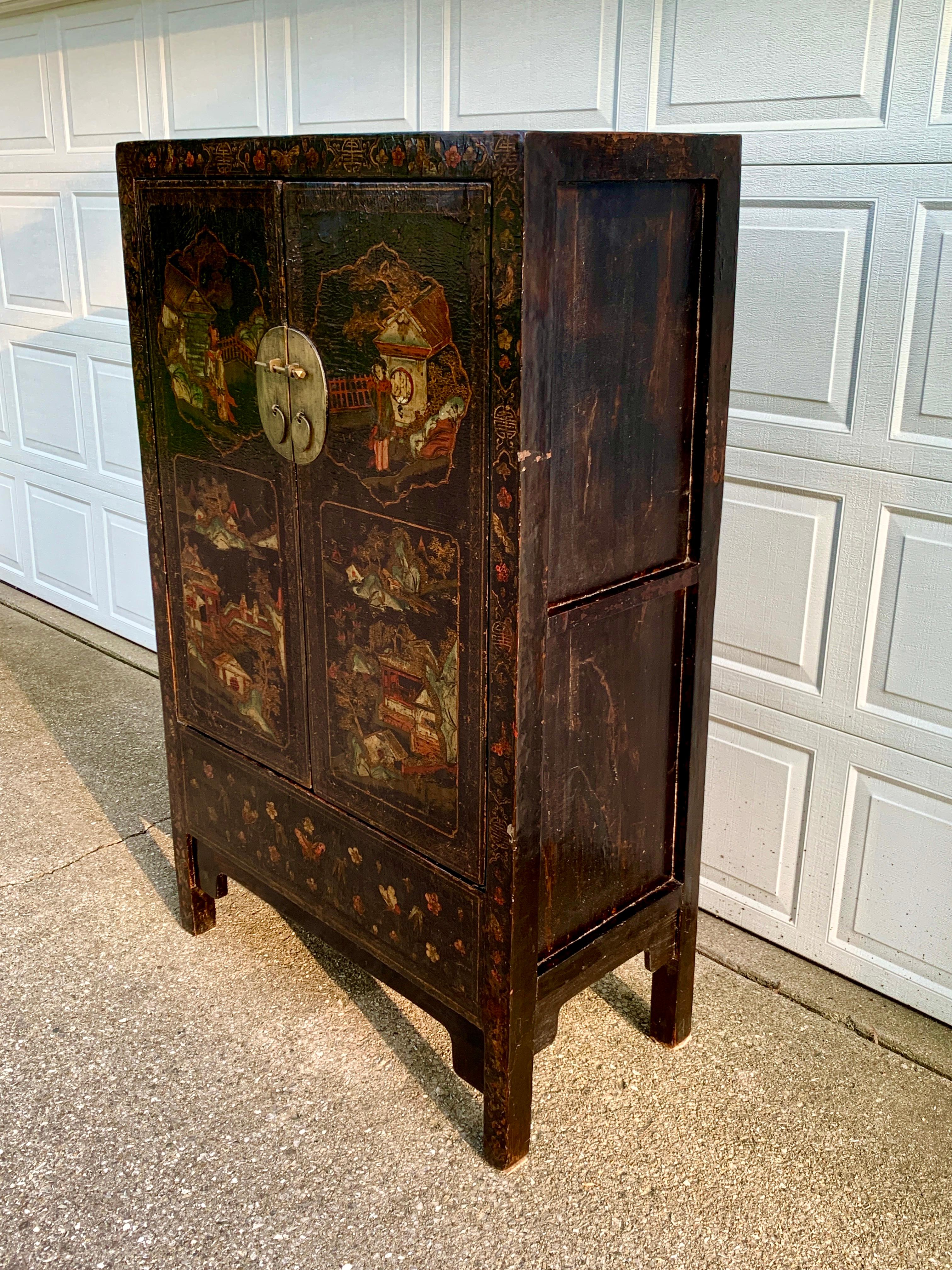 A stunning and rare black lacquered Chinese cabinet featuring hand-painted Chinoiserie scenes. The two-door cabinet has two drawers and three shelves inside, along with a lower compartment concealed under a removable panel on the bottom