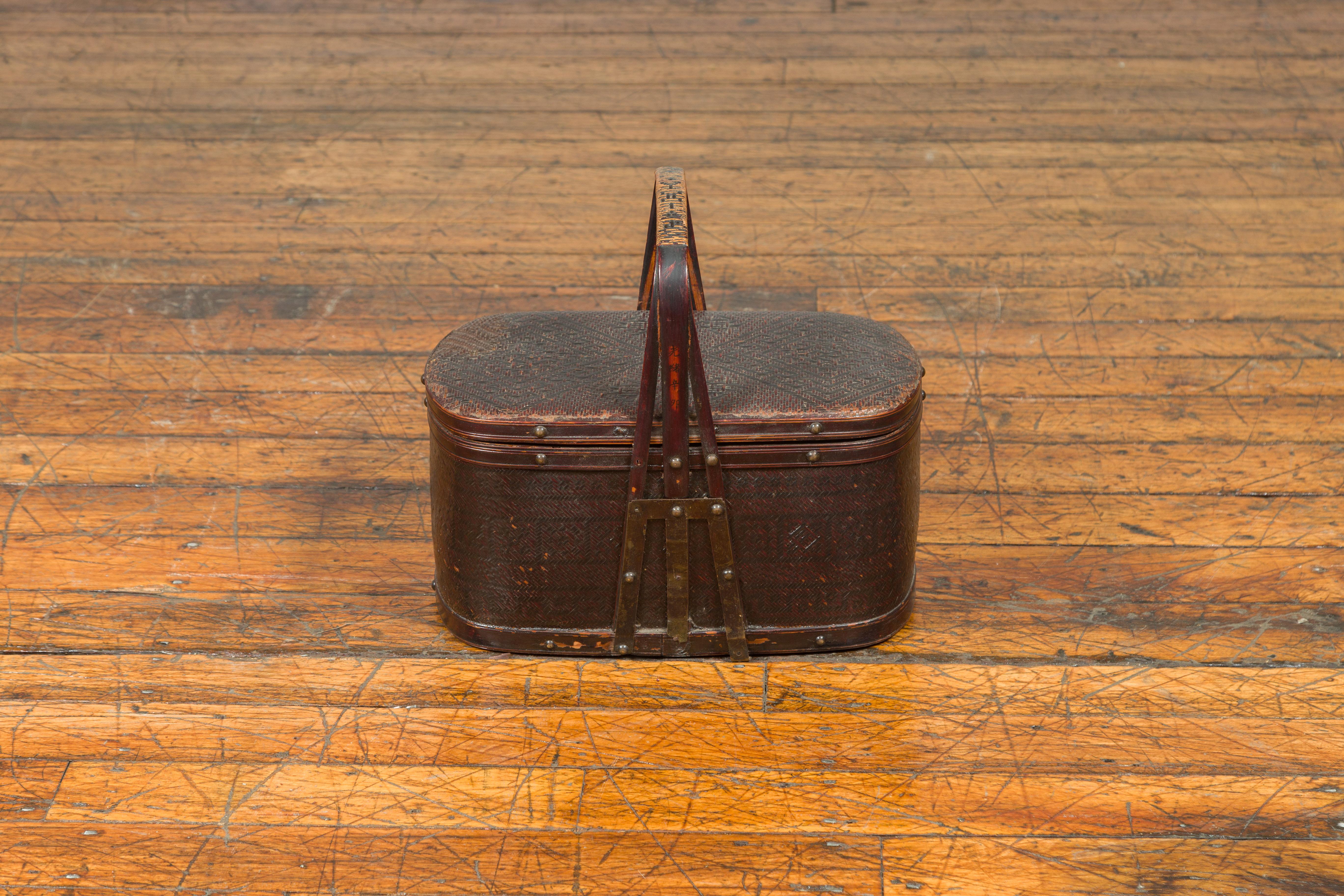 An antique Chinese rattan and bamboo lunch box from the early 20th century, with geometric motifs. This antique rattan and bamboo lunch box from the early 20th century exudes rustic charm and authentic craftsmanship. Featuring an oval shape, the box