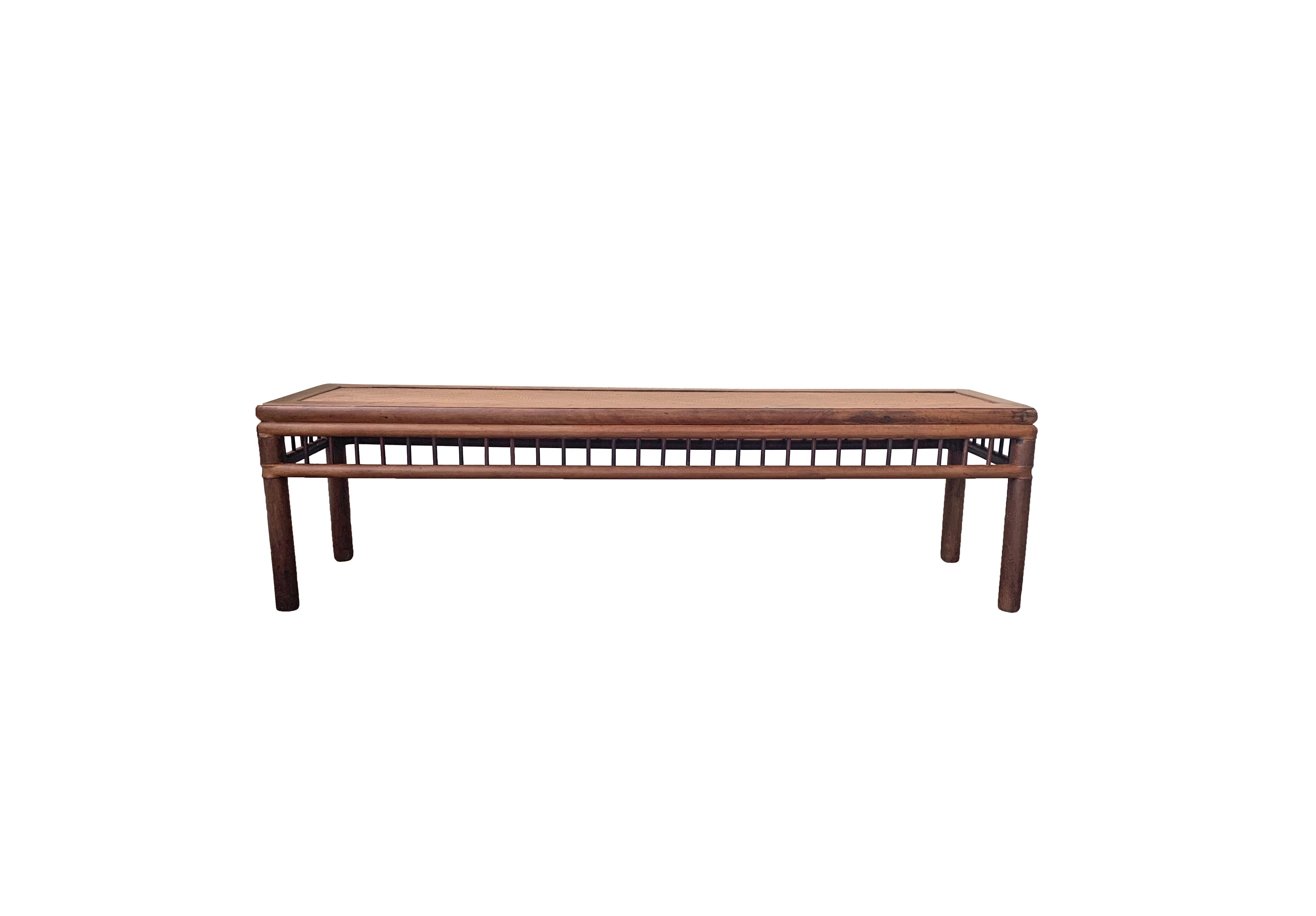 This Chinese long Bench from the Qing Dynasty features wonderfully round legs and vertical supports. It features a wonderfully elongated shape and lacquer finish. Crafted from elm wood it features a rattan seat and age related patina and textures.