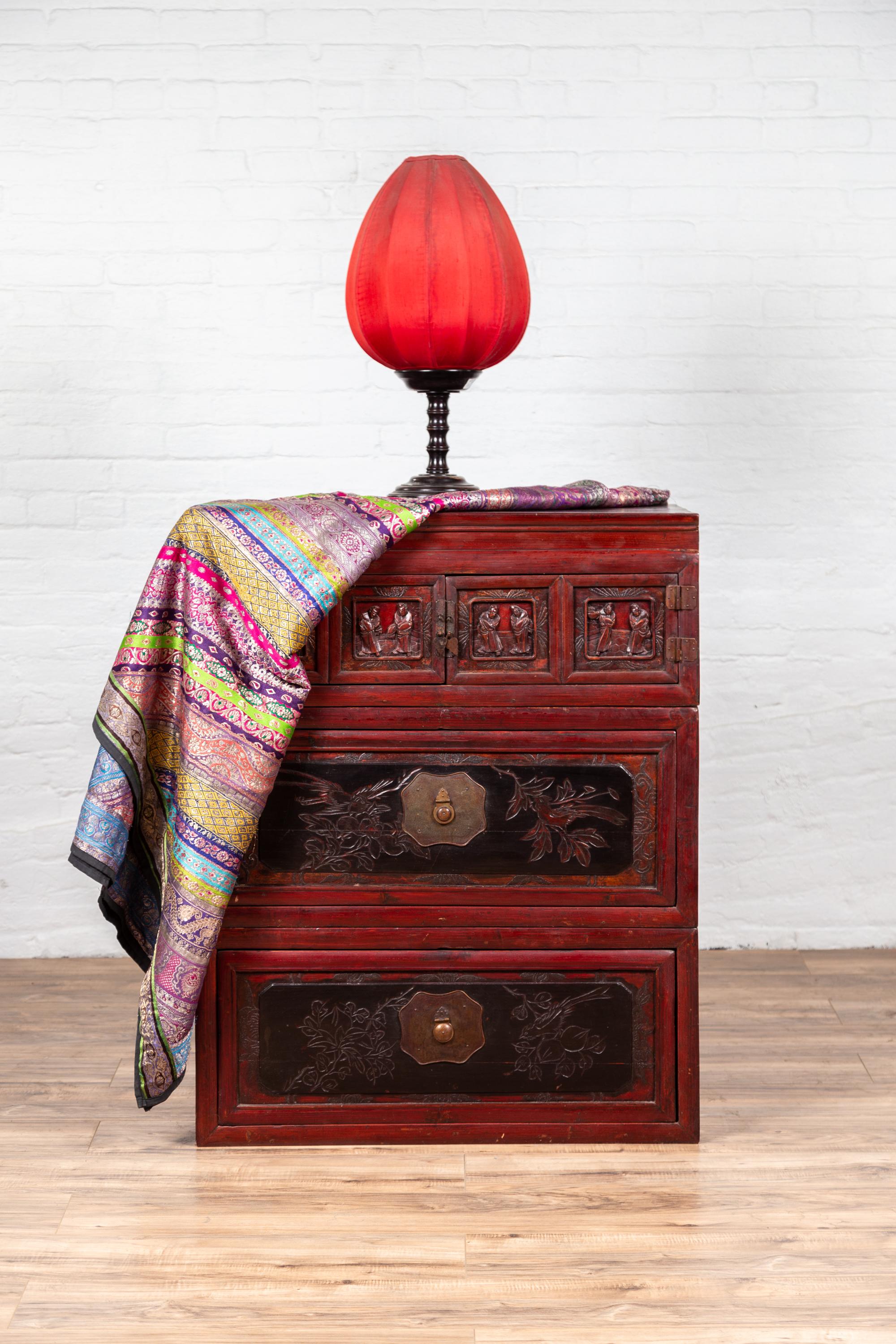 A Chinese antique red and black lacquered three-section chest with carved figures. Featuring a lovely red lacquered body, beautifully accented with black tones, this linear Chinese chest is made of three independent sections. The upper part is