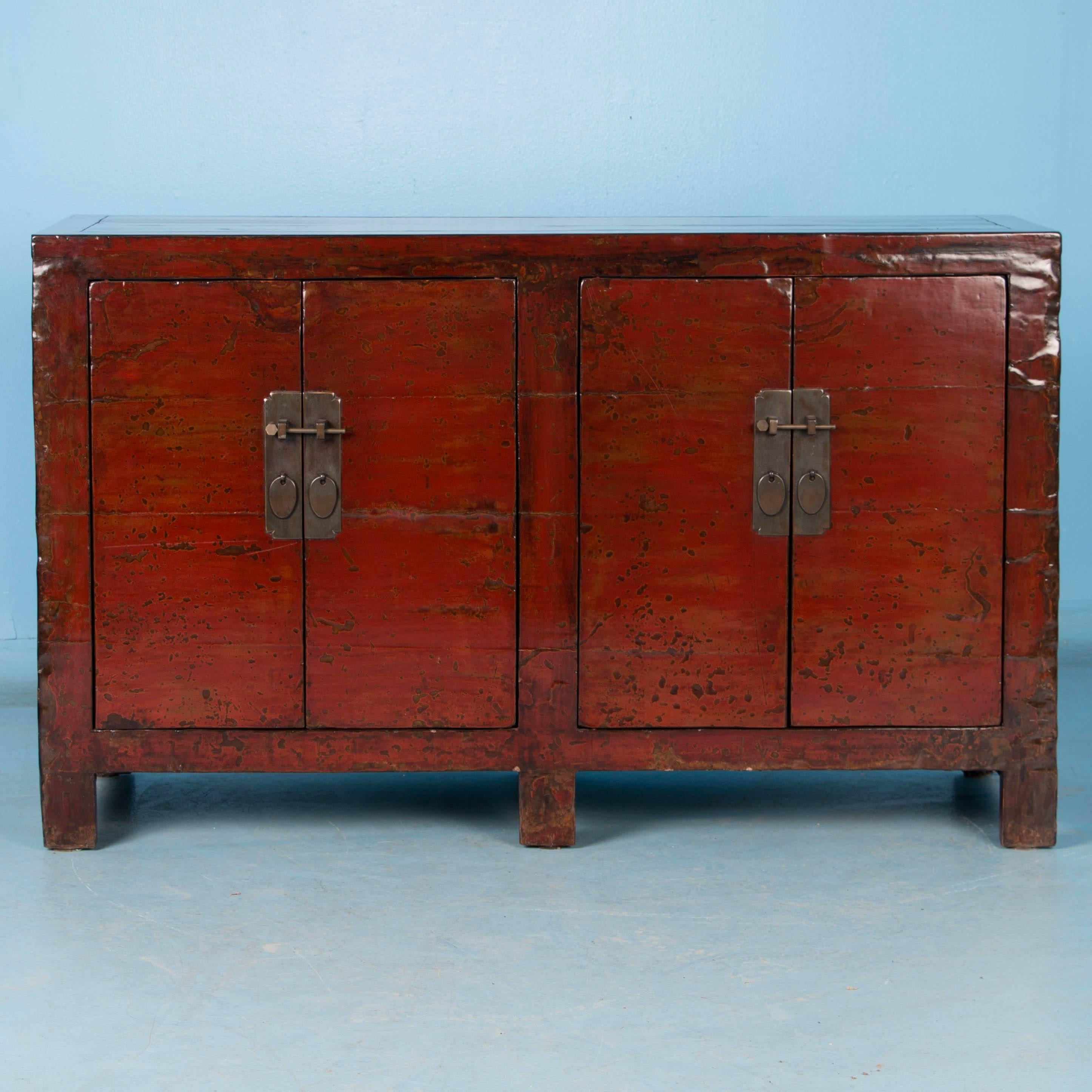 The deep red color of this Chinese four door cabinet is enhanced by it's highly polished lacquered finish while the dark maroon sides offer a nice contrast and continue the clean modern look of the piece. Where paint was worn down through the years,