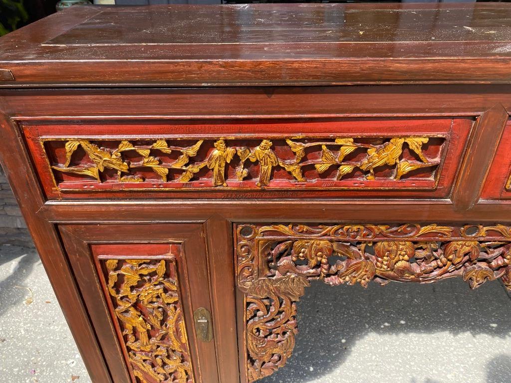 Cette table d'autel rouge antique laquée est fabriquée à la main en bois dur:: avec des motifs percés sur le tablier et des panneaux dorés à la feuille sur le devant 
. Une porte de chaque côté du fond et des compartiments spacieux sont fermés de