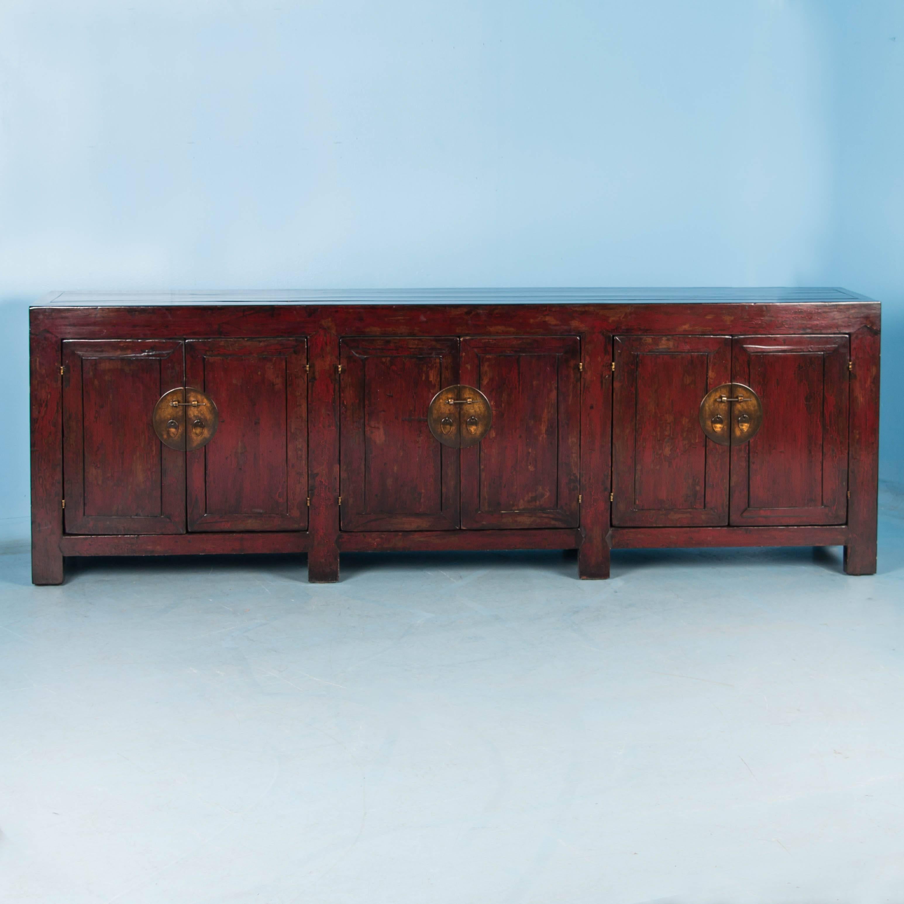 The rich color and finish on this stunning antique Chinese sideboard is a combination of elements. The original red painted finish has been worn down in places to reveal the natural elm wood below. The entire sideboard has a lacquered finish, which