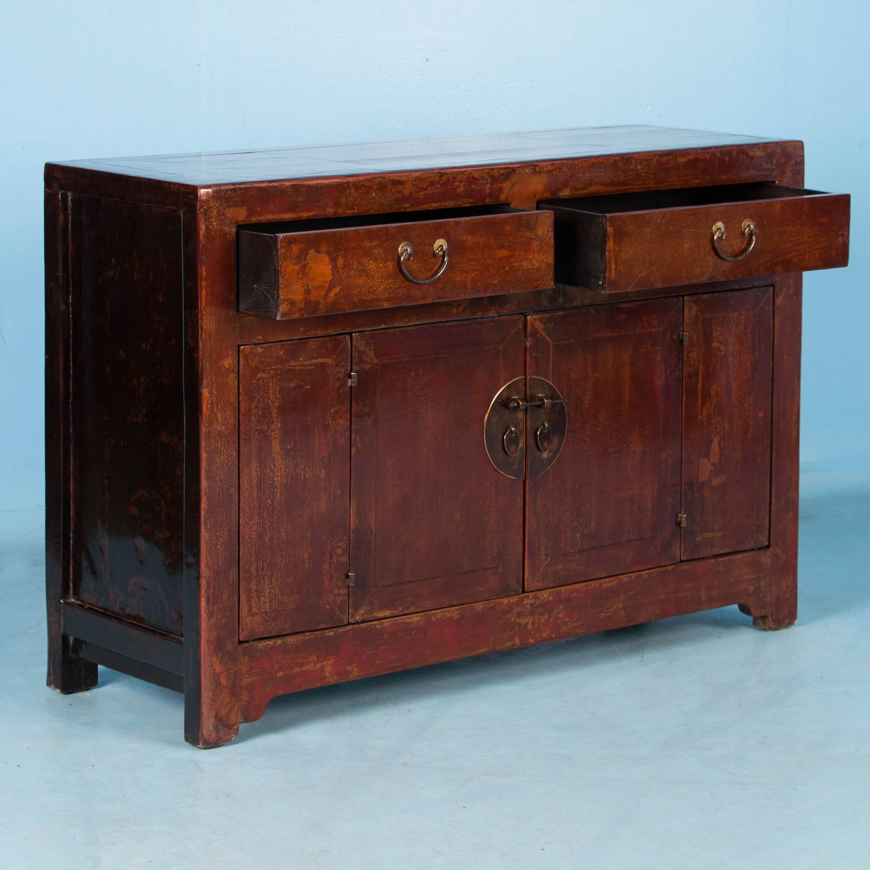 Beautiful and versatile, this painted Chinese lacquered cabinet has a lovely aged patina with hints of lighter red and amber beneath a time worn, dark red paint whispering of years gone by. The lacquered finish is highly polished giving the paint