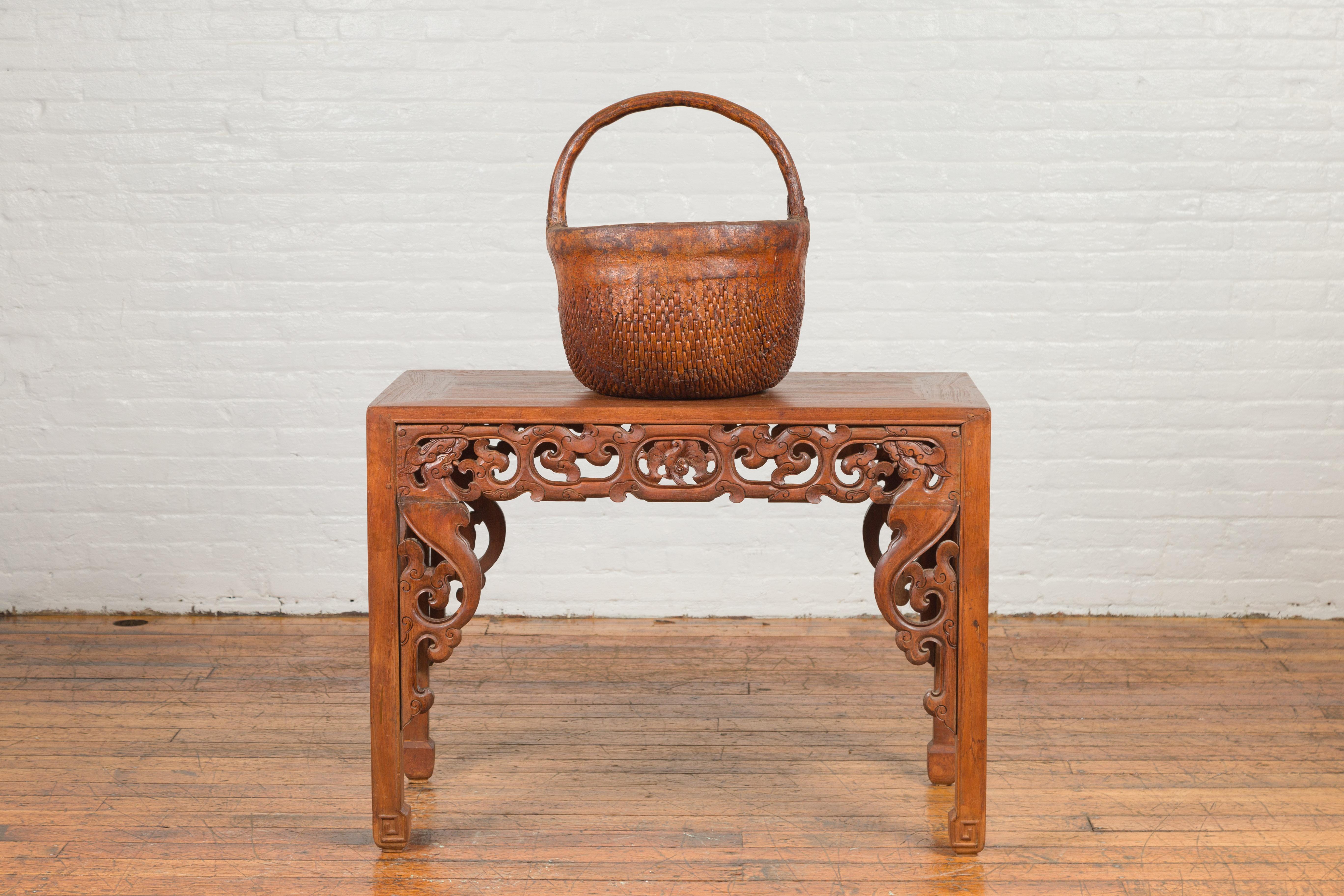 An antique Chinese carrying basket from the 19th century, with intricate woven rattan design. Created in China during the Qing Dynasty, this Chinese carrying basket charms us with its rustic appearance. A large handle is resting upon a rattan body