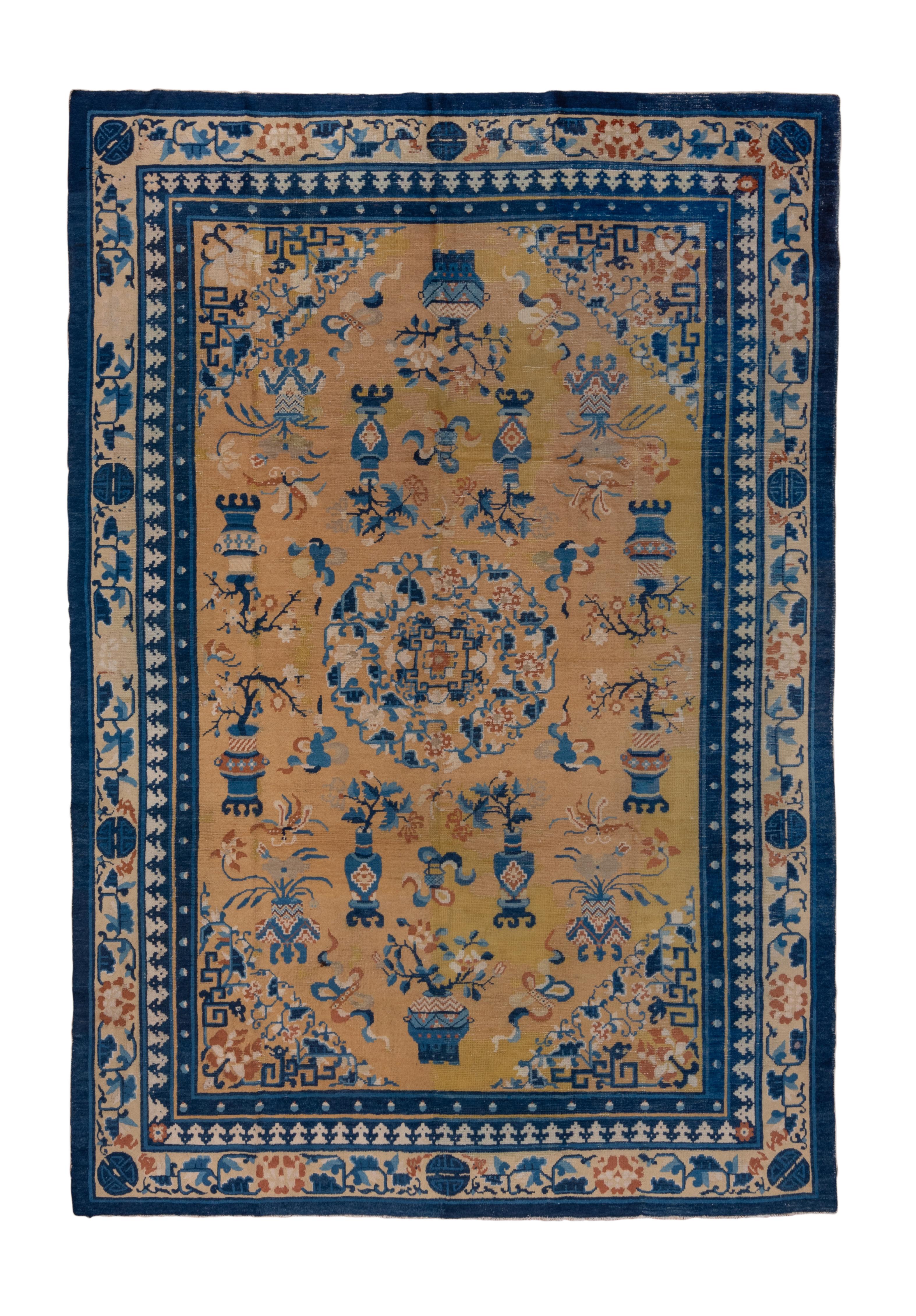 The old gold field shows a round, composite floral medallion, closely supported by vases, cloud bands, and bonsai trees, within triangular dragon fret and flower corners.  Straw main border and inner with a crenellation pattern. Outermost dark blue