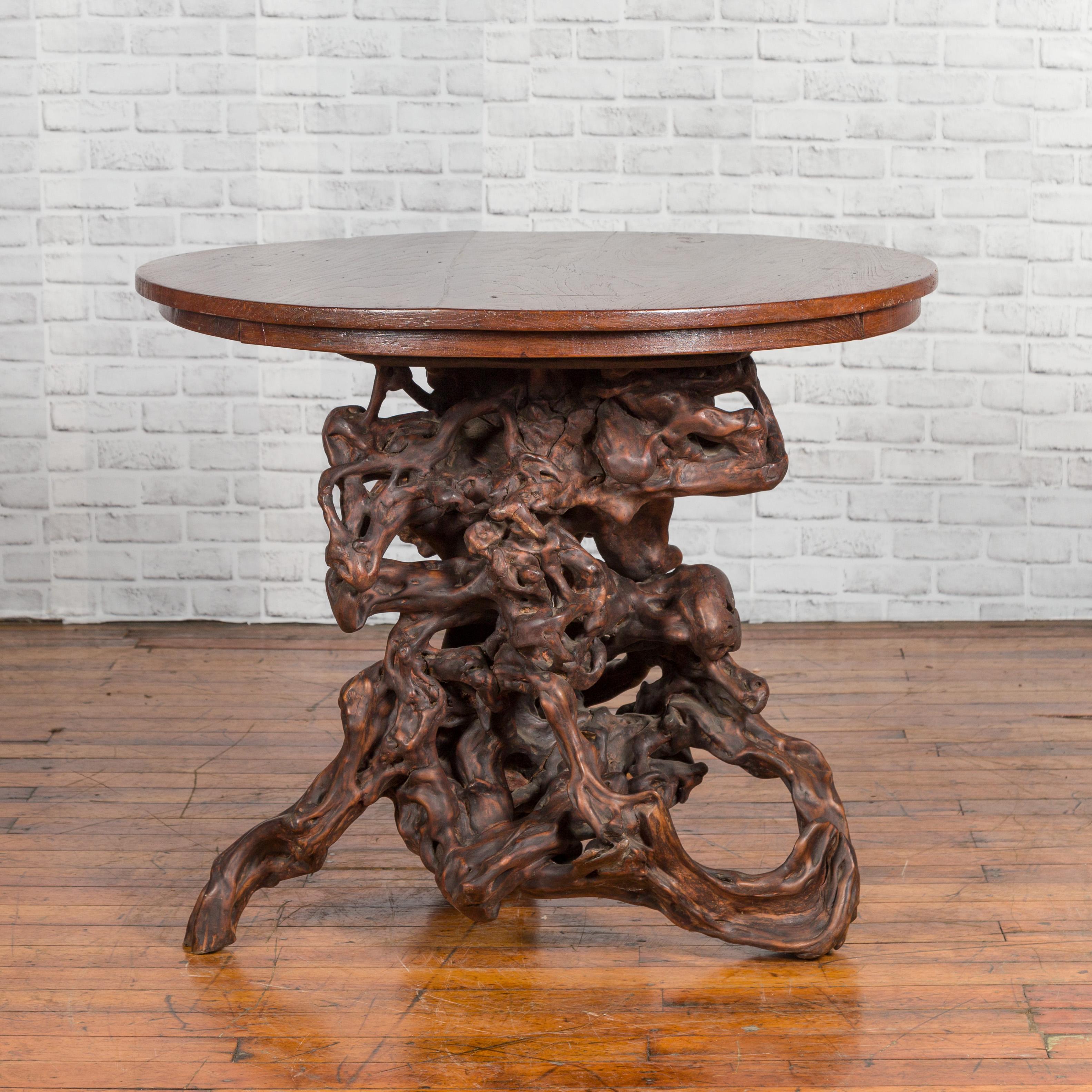 A small Chinese antique root table from the early 20th century, with circular top. Created in China, this center table features a circular planked top sitting above a striking root base, whose knotted quality creates a perfect contrast with the