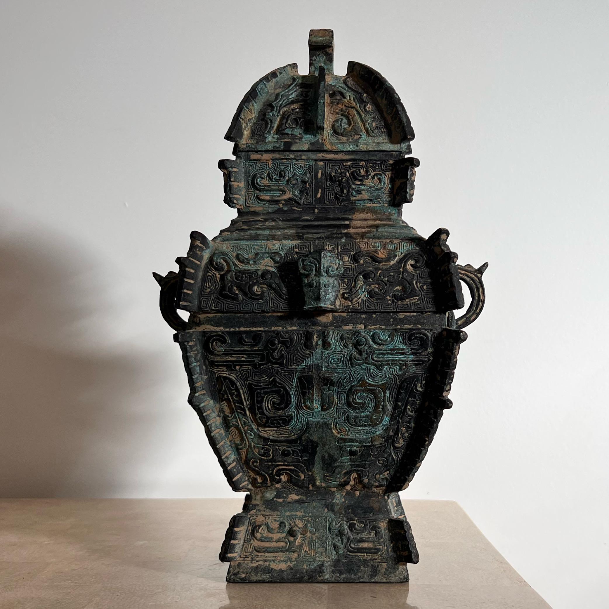 A guang - an Antique Chinese Shang Dynasty style cast bronze ritual vessel, 16th century. Each side of this striking piece is cast with taotie masks and archaic birds, and the two outer planes are flanked by beast loop handles and vertical notched