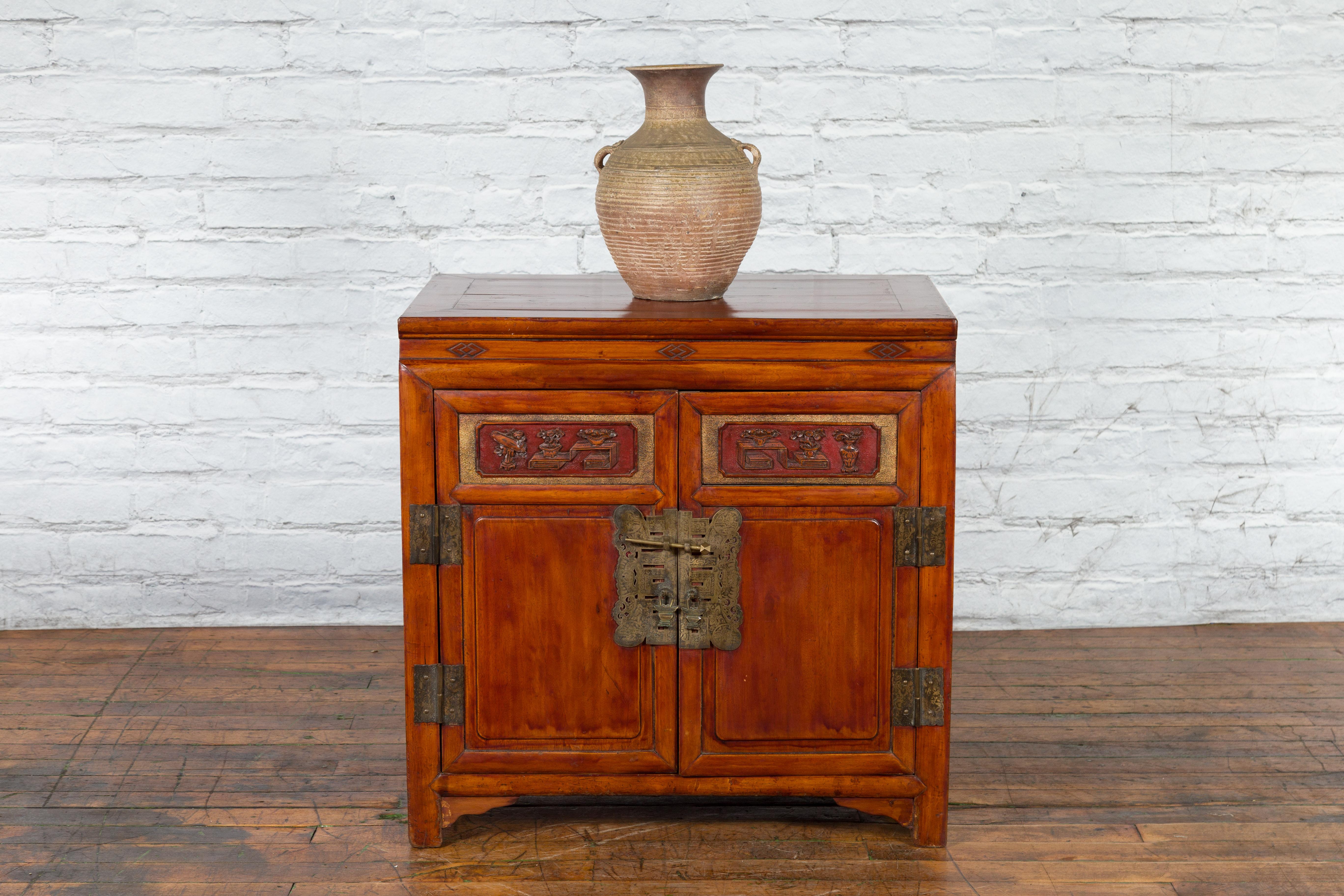 A Chinese antique side cabinet from the early 20th century with brown lacquer, carved panels, gilded accents, hidden drawers and brass hardware. Created in China during the early years of the 20th century, this side cabinet features a rectangular