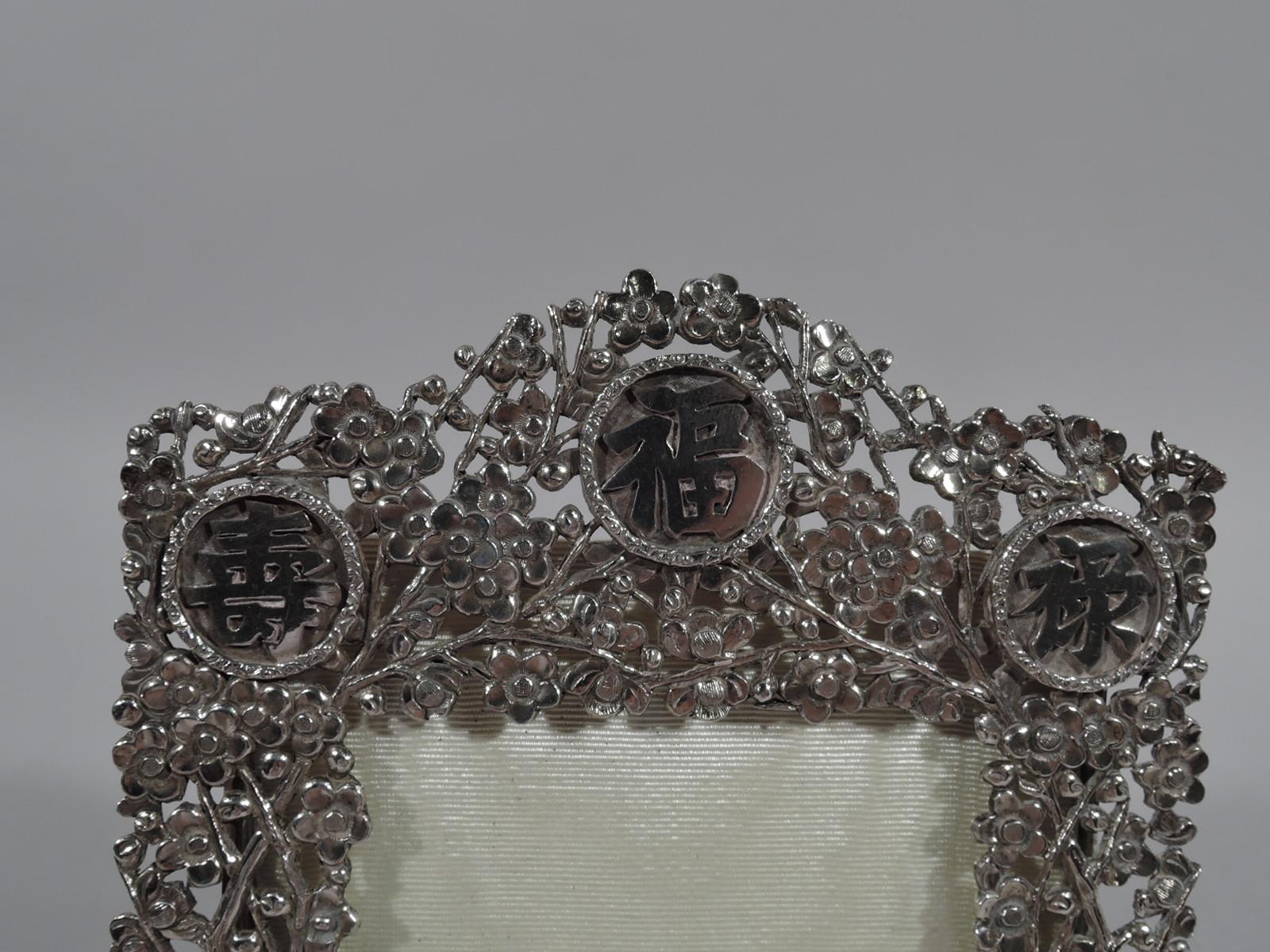 Chinese export silver picture frame. Rectangular window in same surround with arched top comprising pierced and dense blossoming prunus branches with scrolled branches at base and 3 rondels inset with Chinese characters at top. With glass, silk